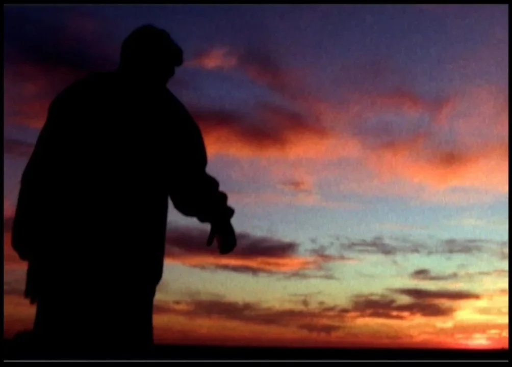 Silhouette of a person standing against a colorful sunset sky with clouds in shades of purple, orange, and pink.