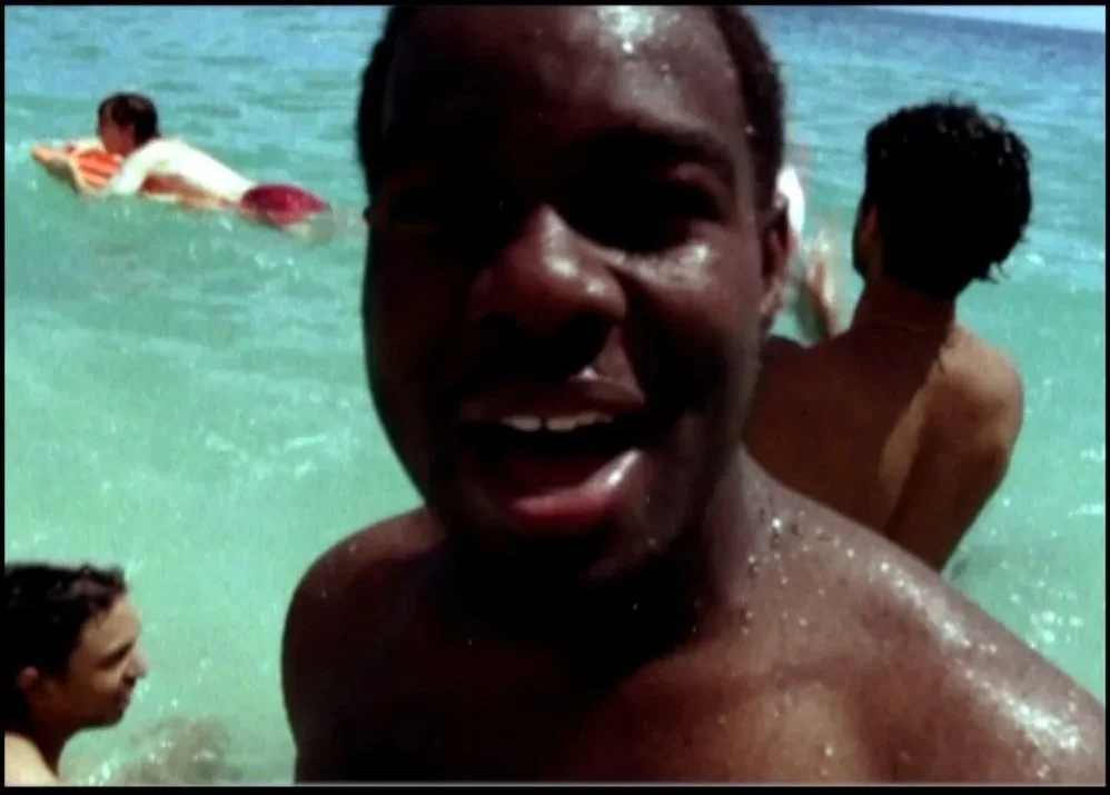 A group of people enjoying themselves at the beach, swimming in the ocean, with one man smiling and close to the camera.