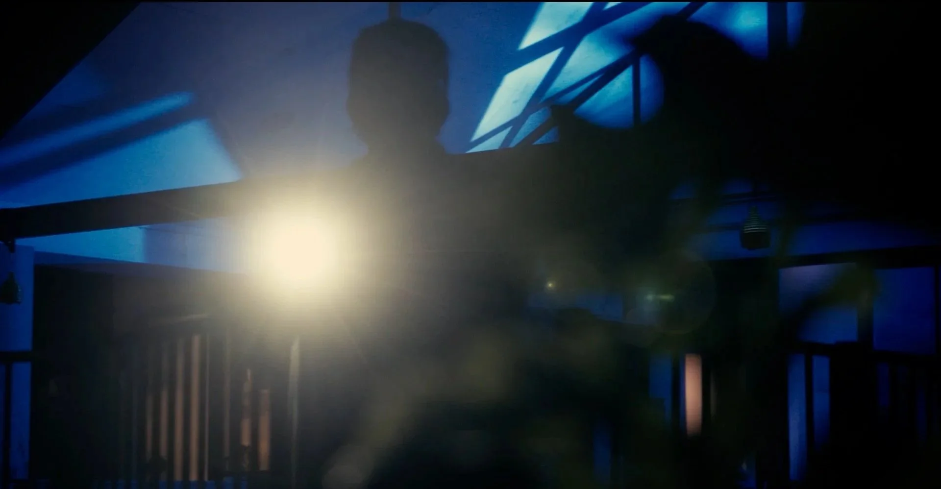 Silhouette of a person standing in front of a bright light with blue and dark shadows, indoors with structural beams visible.