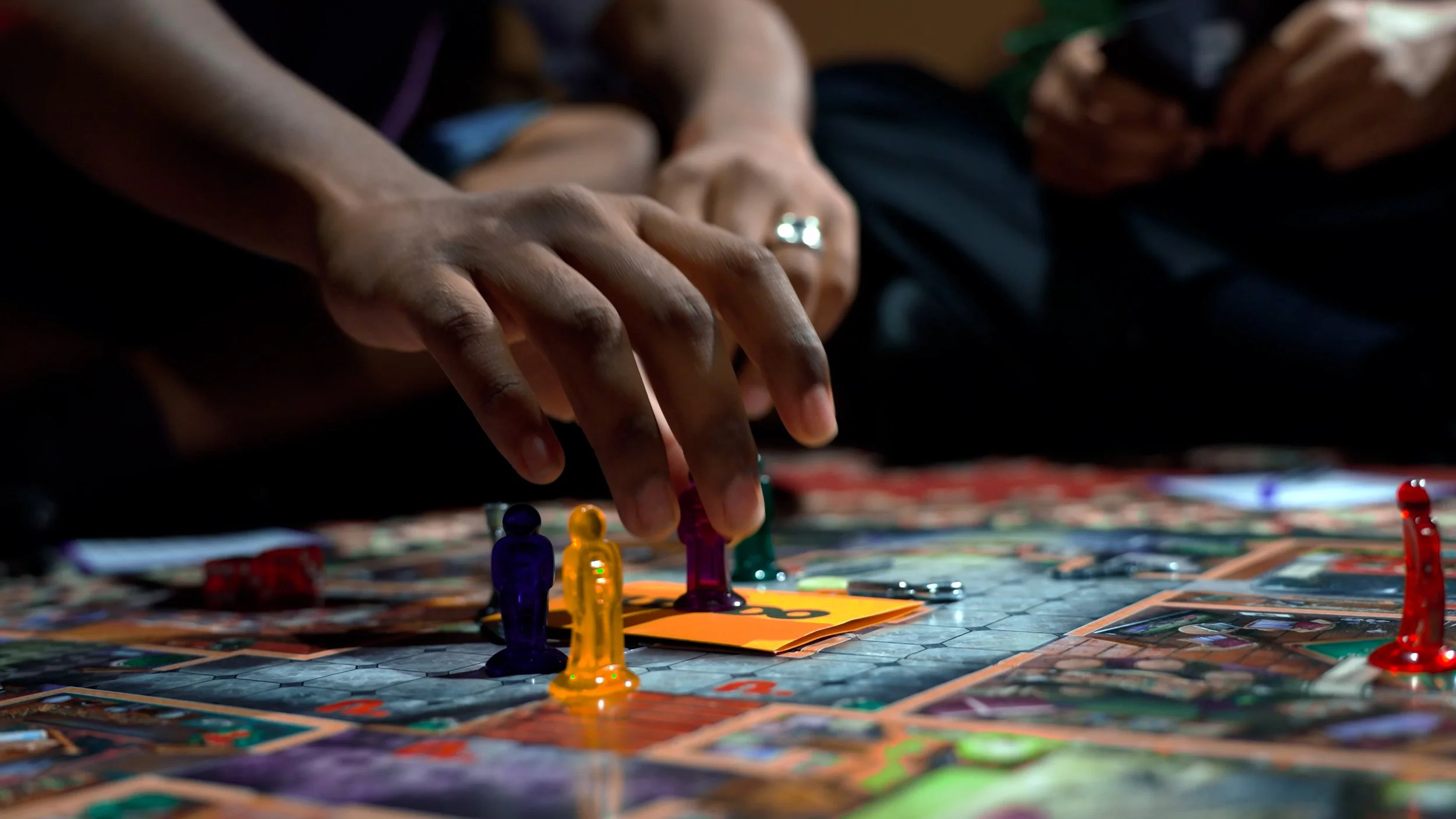 Close-up of a person's hand moving colorful game pieces on a board during a board game.
