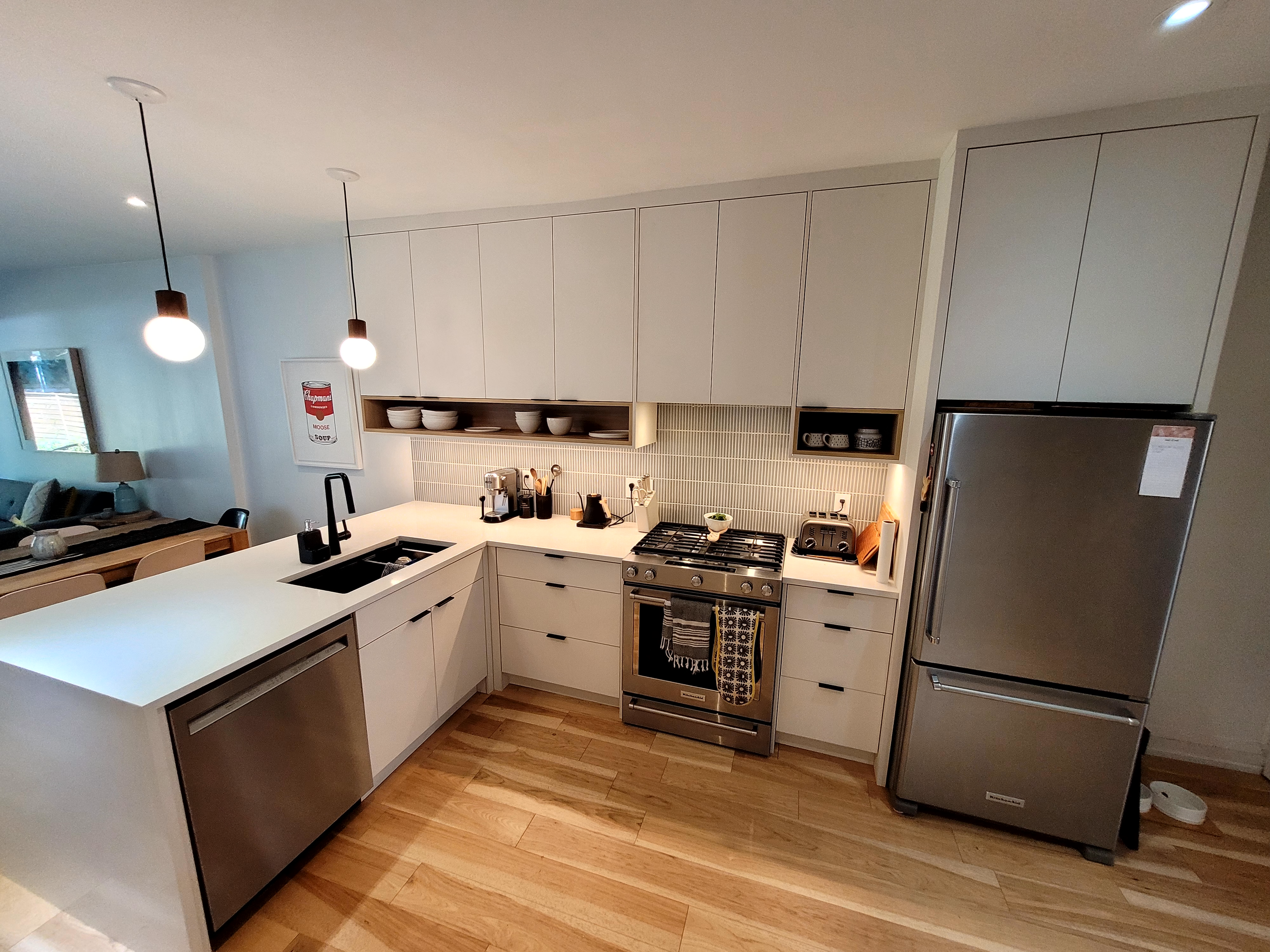 Modern kitchen with white cabinets, stainless steel appliances, wooden floor, and pendant lighting, adjacent to a dining area with a wooden table and chairs.