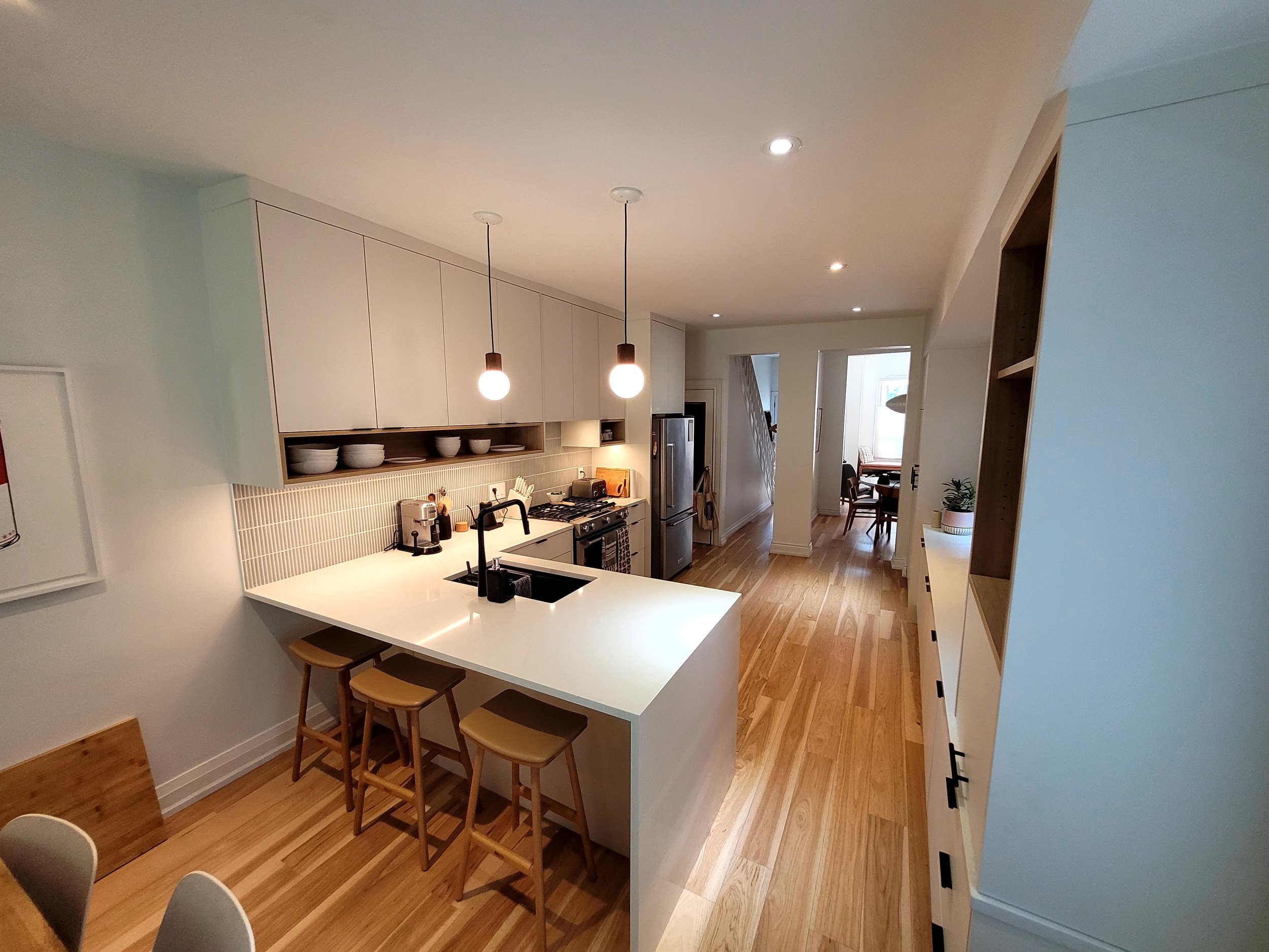 Modern kitchen with white cabinets, white island with barstools, pendant lights, and hardwood floors, adjacent to dining area with table and chairs.
