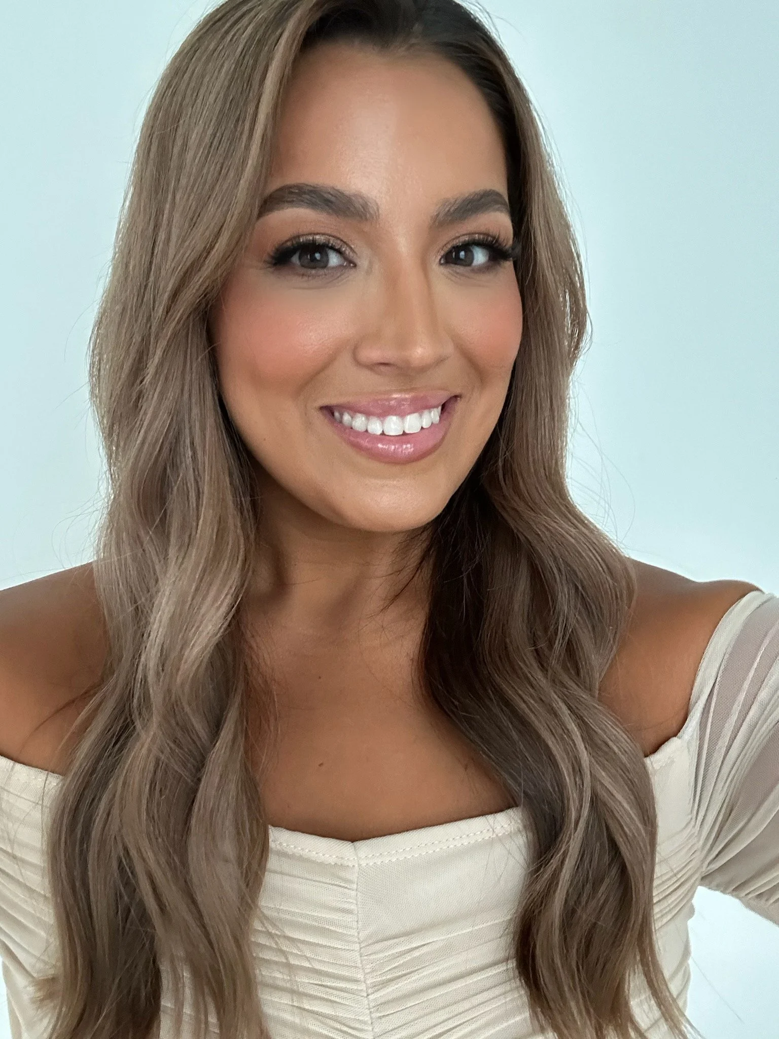 Smiling woman with long brown hair wearing an off-the-shoulder white top