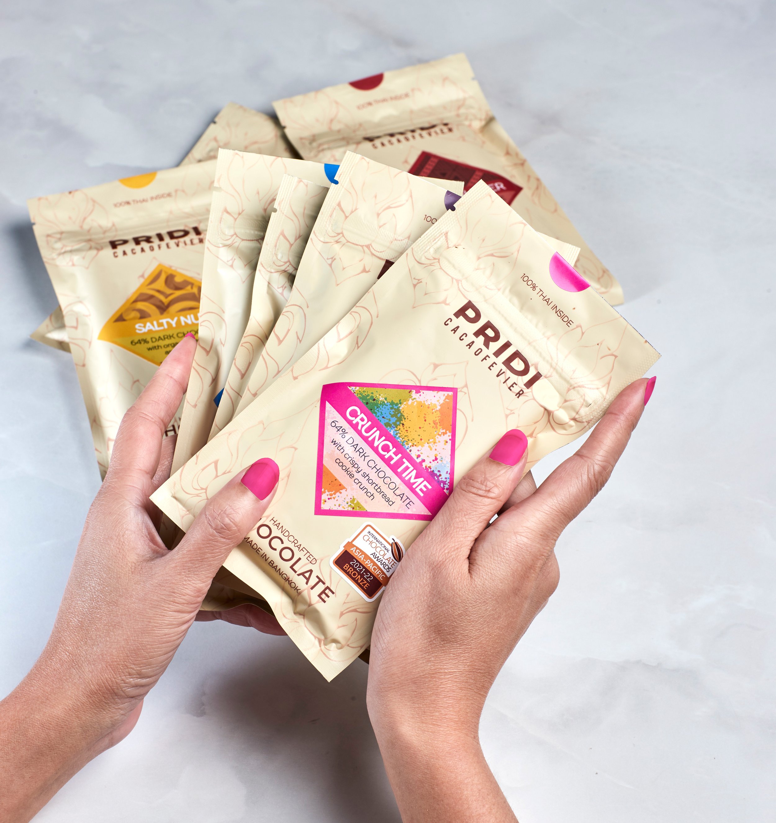 Person holding assorted chocolate packaging from PRIDI Cacaofevier with colorful labels
