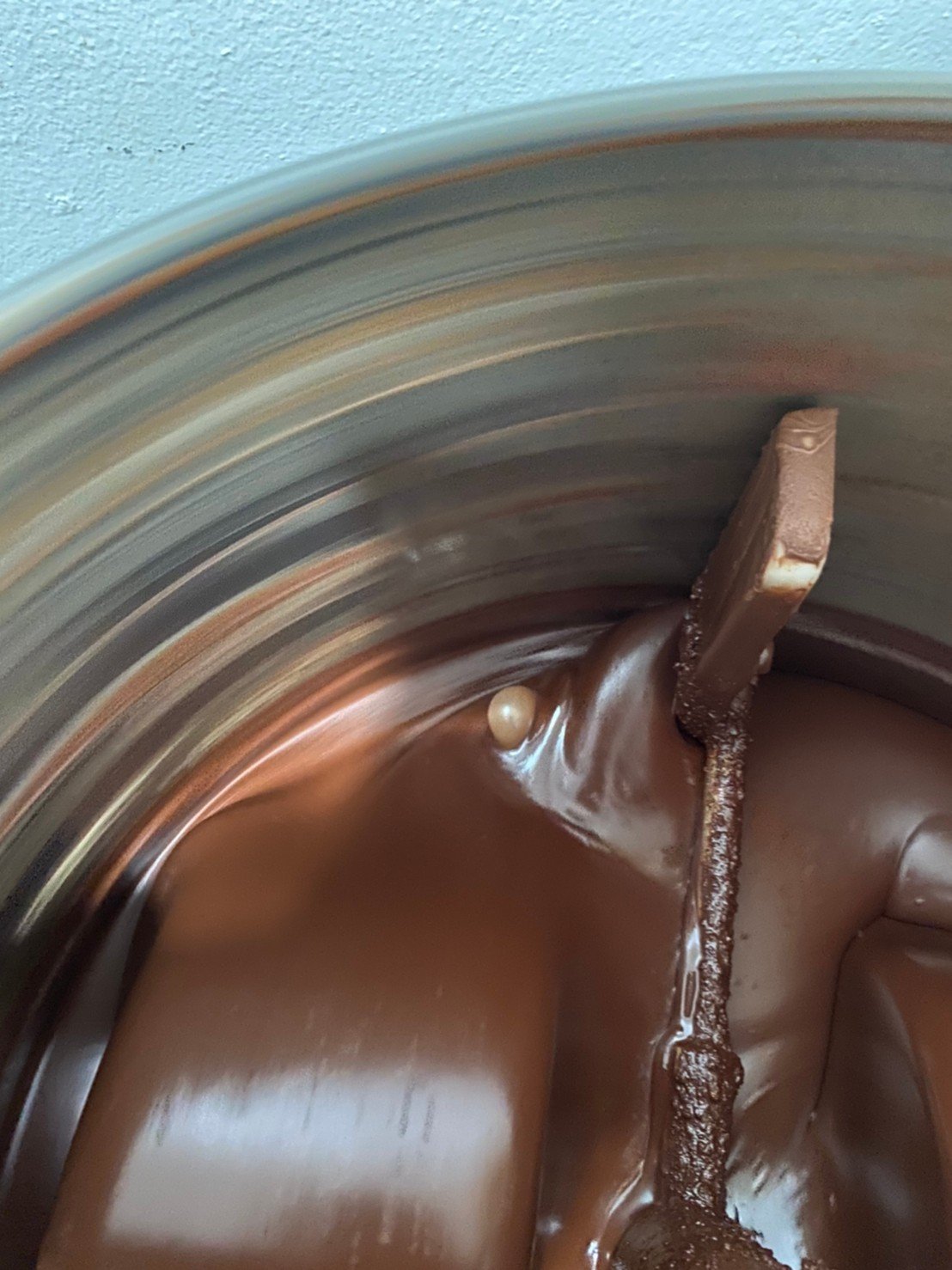 Close-up of chocolate being stirred in a metal mixing bowl with a spatula.