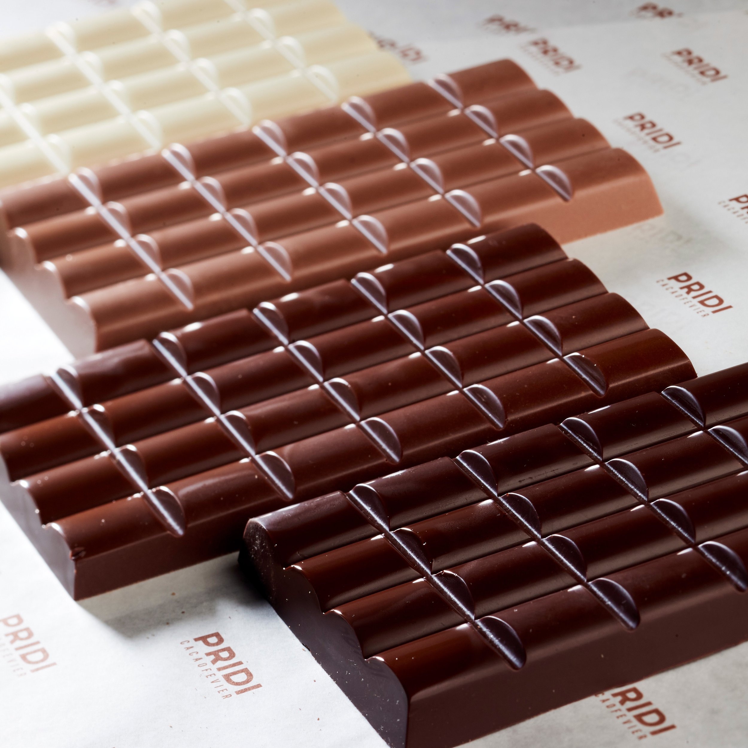 Assorted chocolate bars in varying shades, displayed on paper with 'Pridi' logo.
