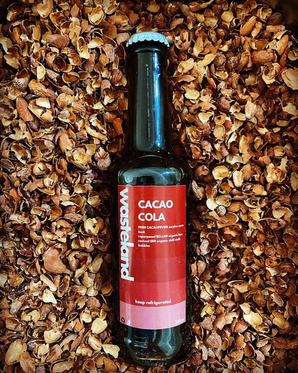 Bottle of PRIDI Cacaofevier Wasteland Cacao Cola resting on cocoa husks
