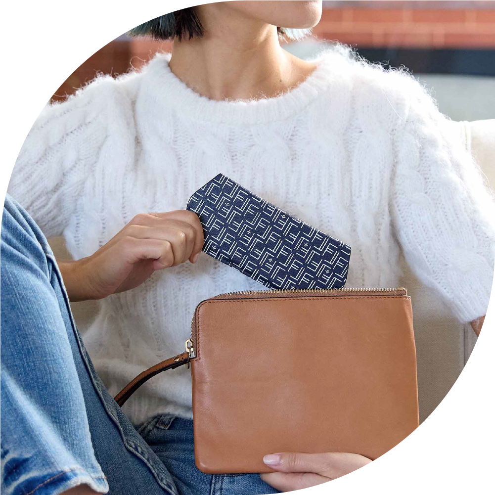 A woman in white is pulling a blue Fox and Leo glasses case out of a tan bag.