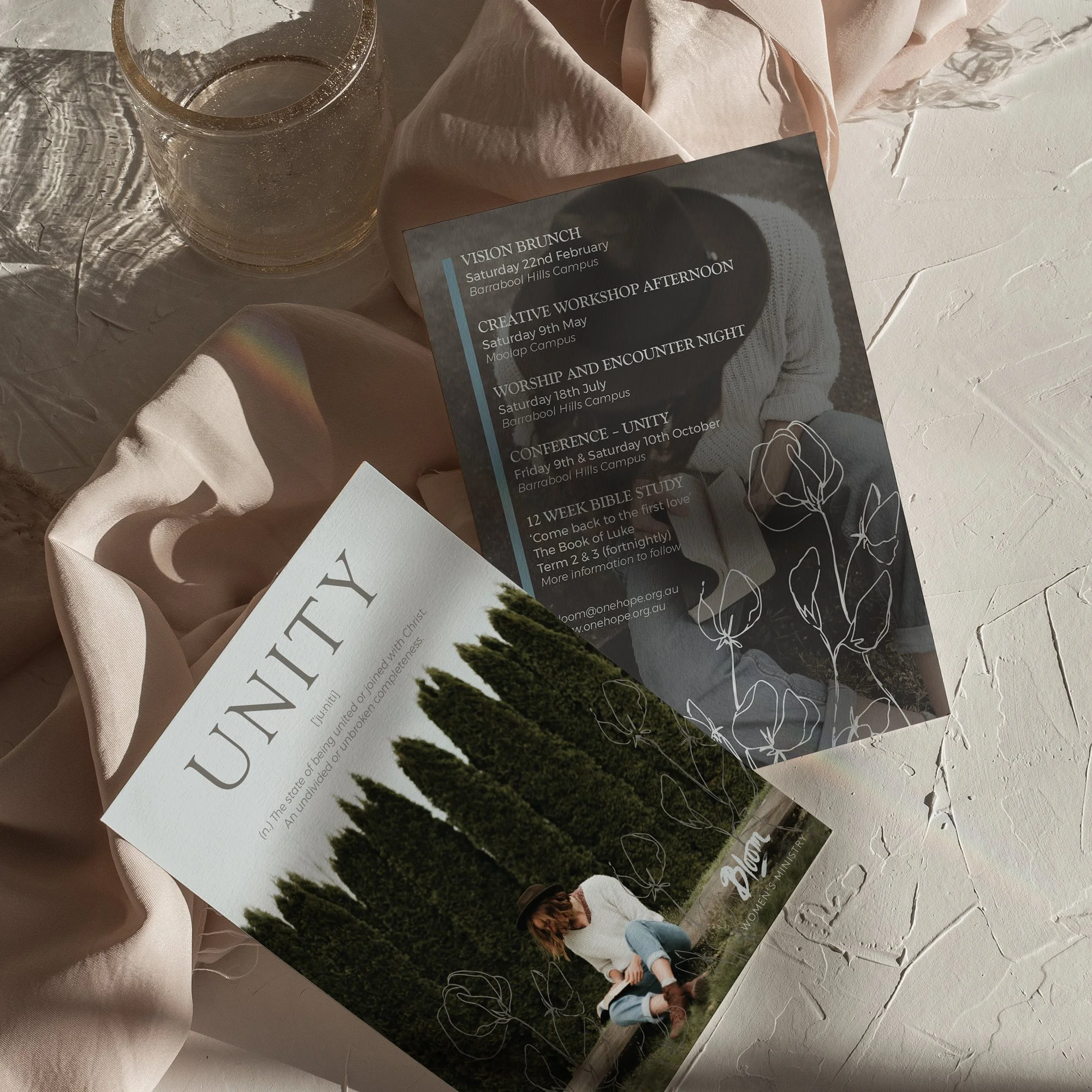 Two event flyers, revealing the front and back of an event promotion, resting on a soft fabric background.