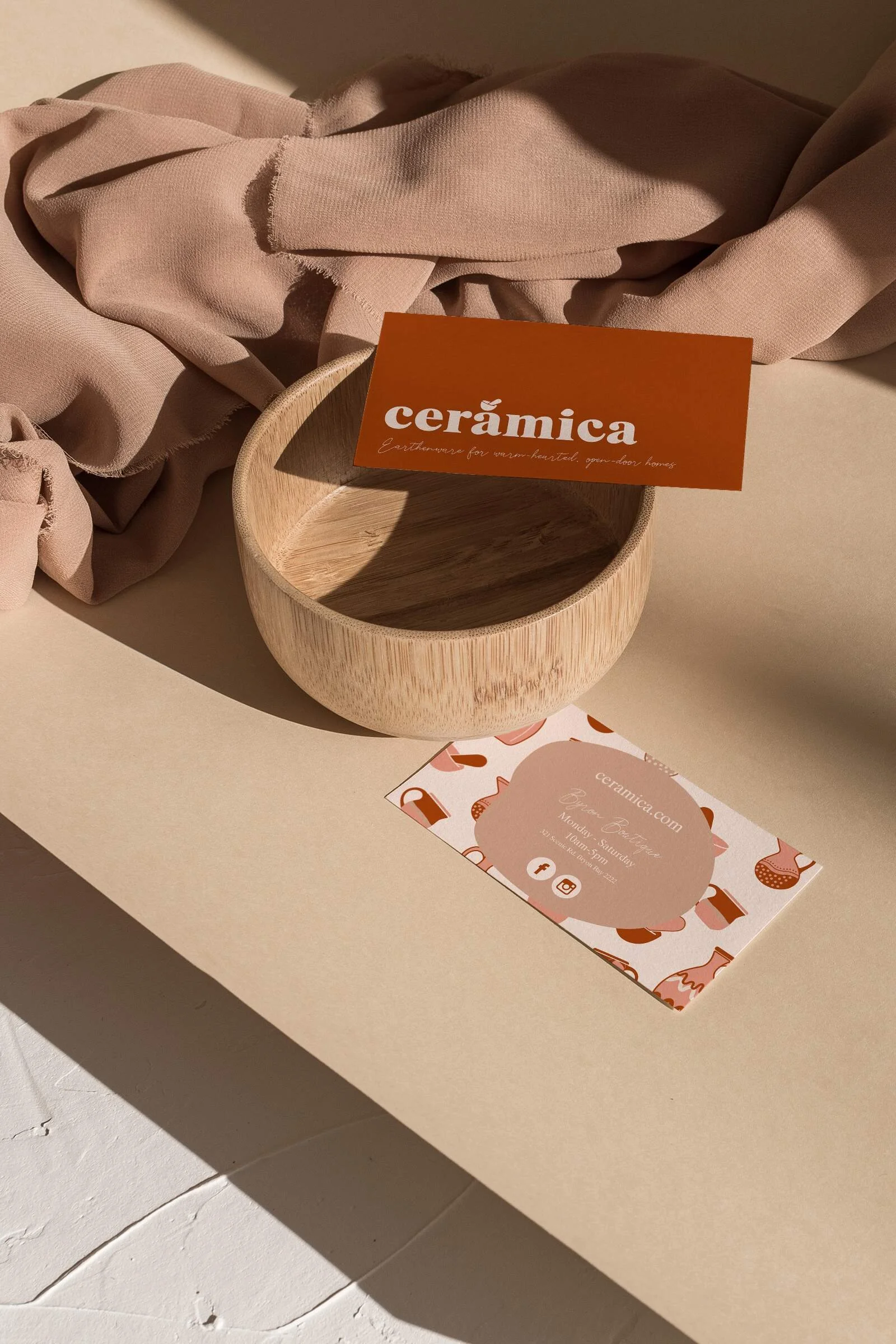 The front and back of a illustrative, rust-coloured Ceramica business card, displayed on a wooden bowl and bench.