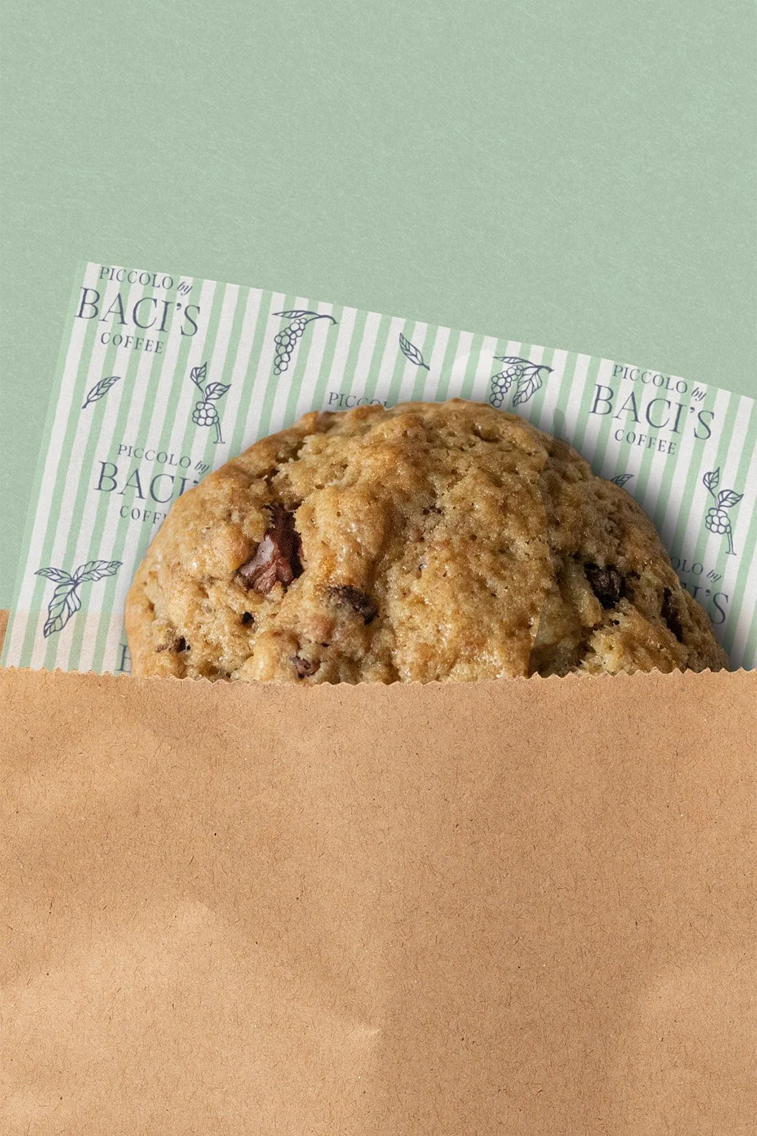Chocolate chip cookie within a brown paper bag with Piccolo by Baci's Coffee tissue paper behind it.