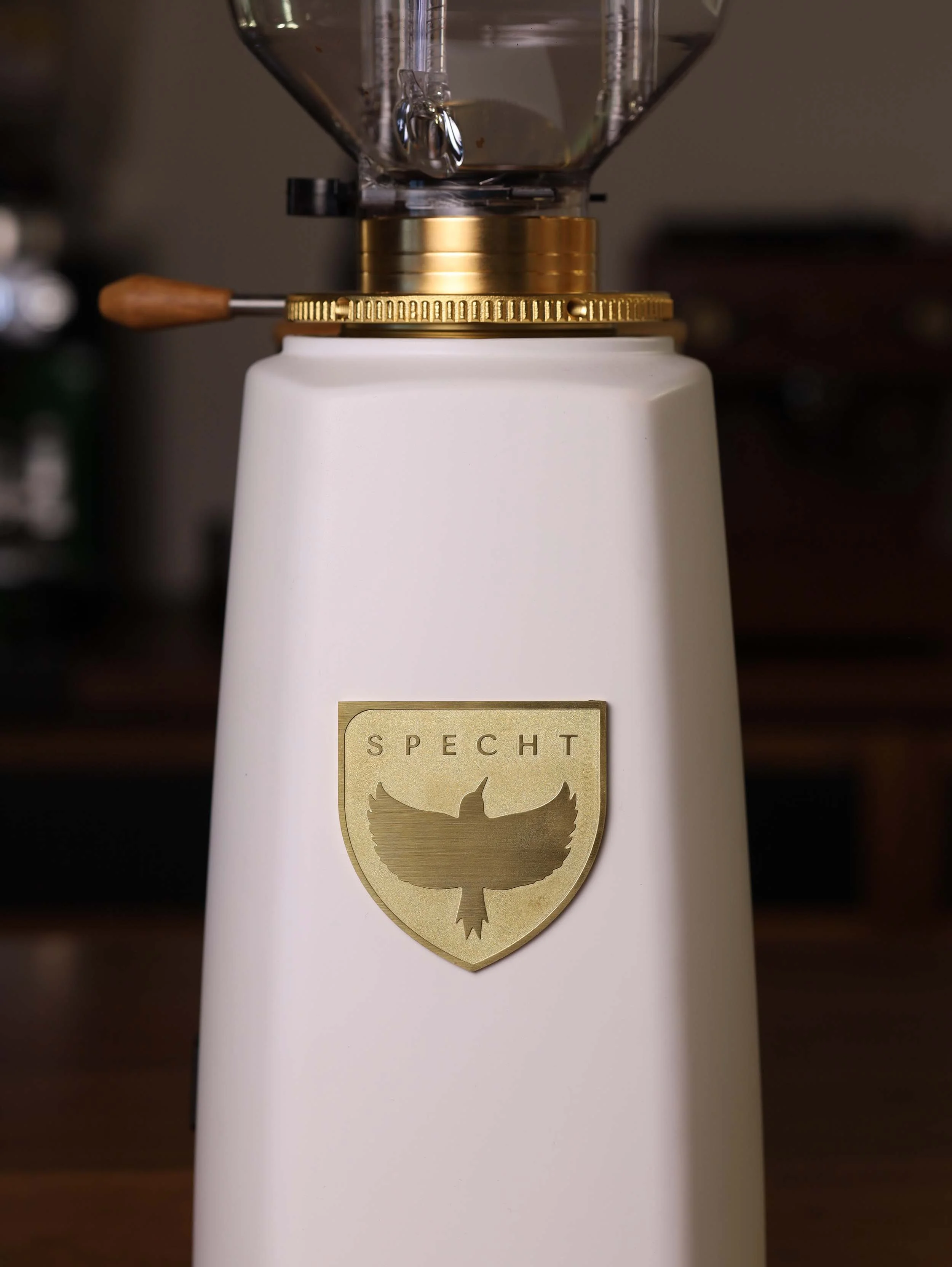 White coffee grinder with a gold Specht badge on it.