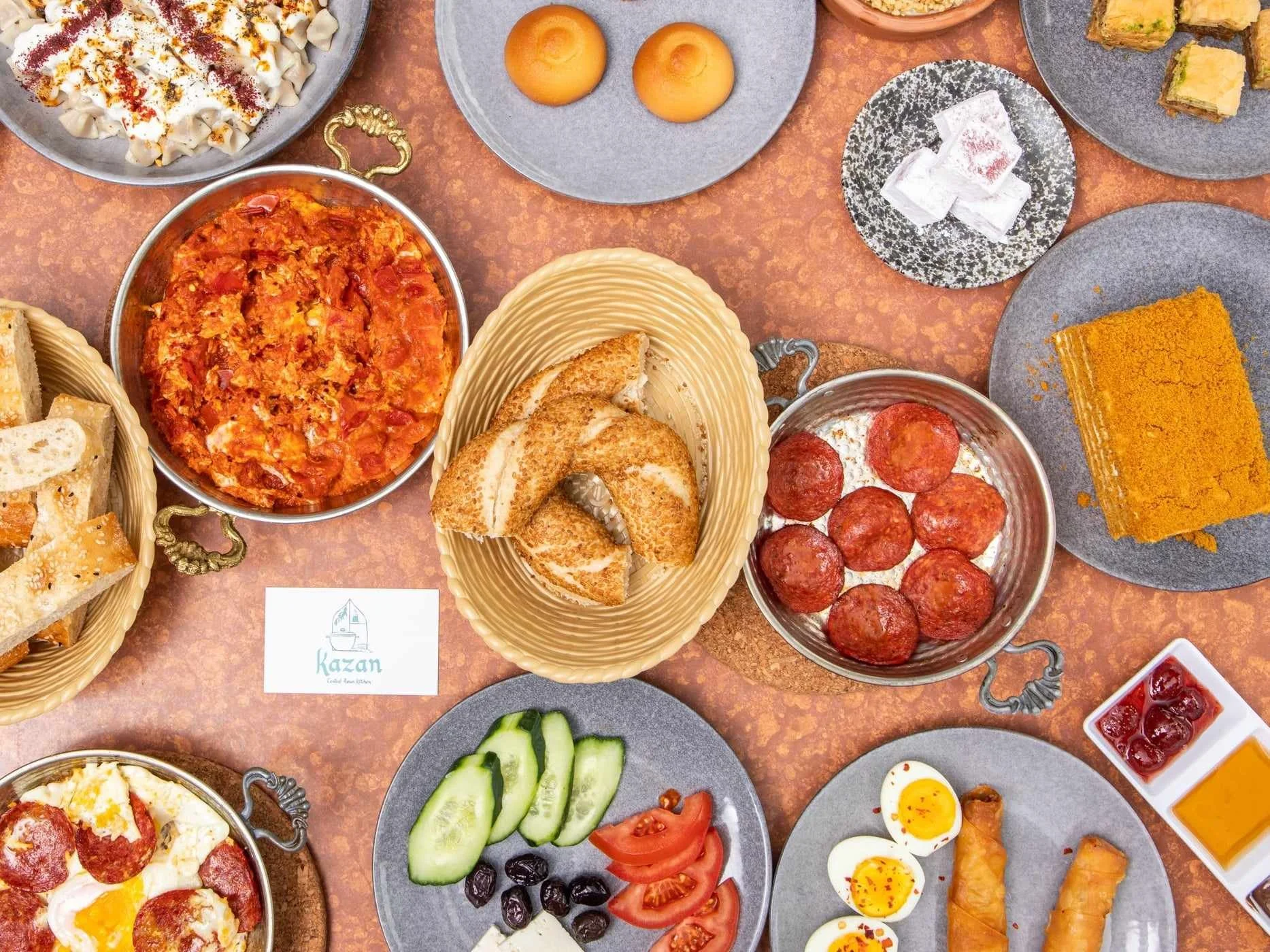 An array of Turkish food spread across a table with a Kazan business card amongst the dishes.