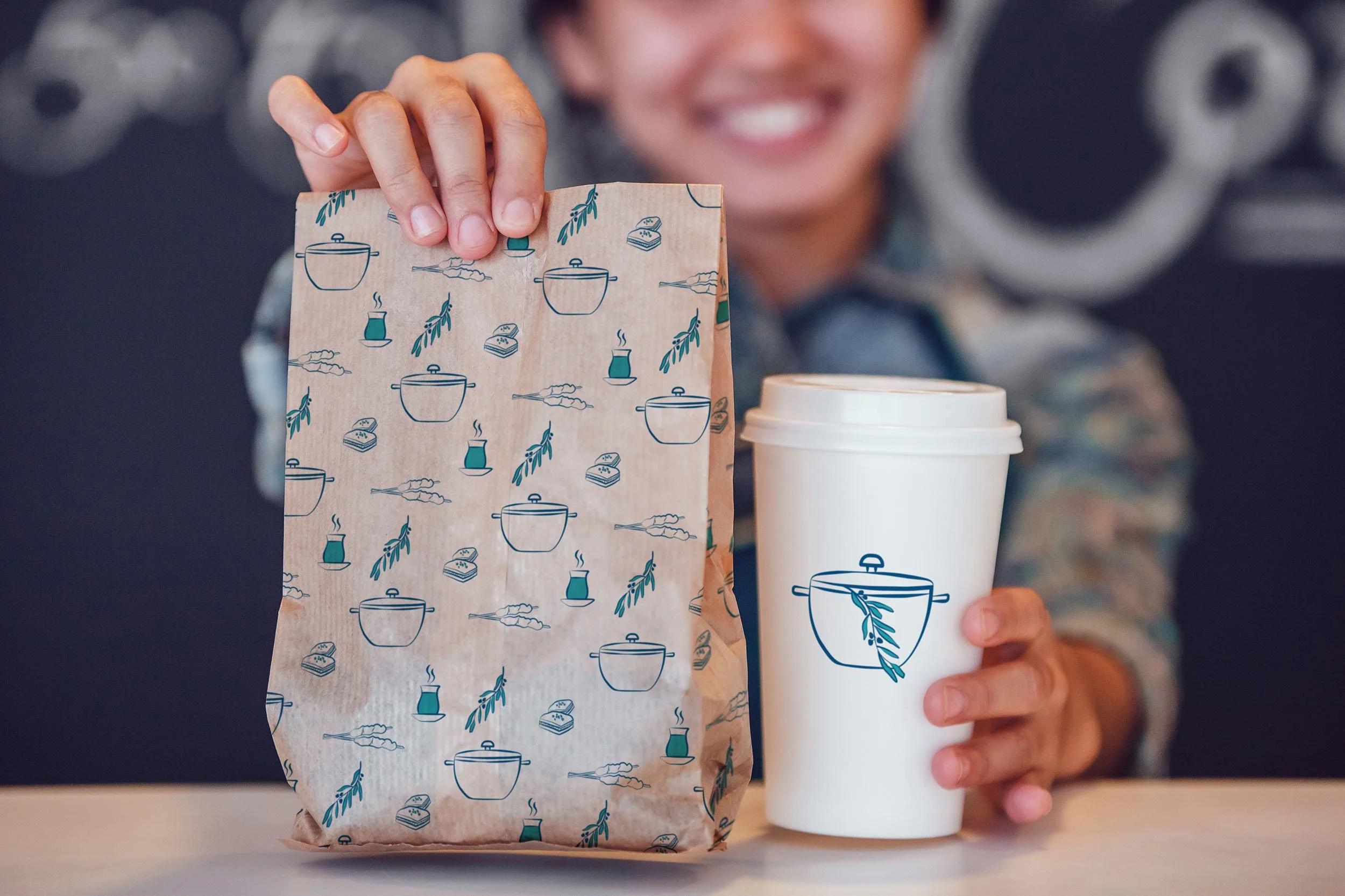 A smiling woman holds branded Kazan paper bag and takeaway coffee cup.