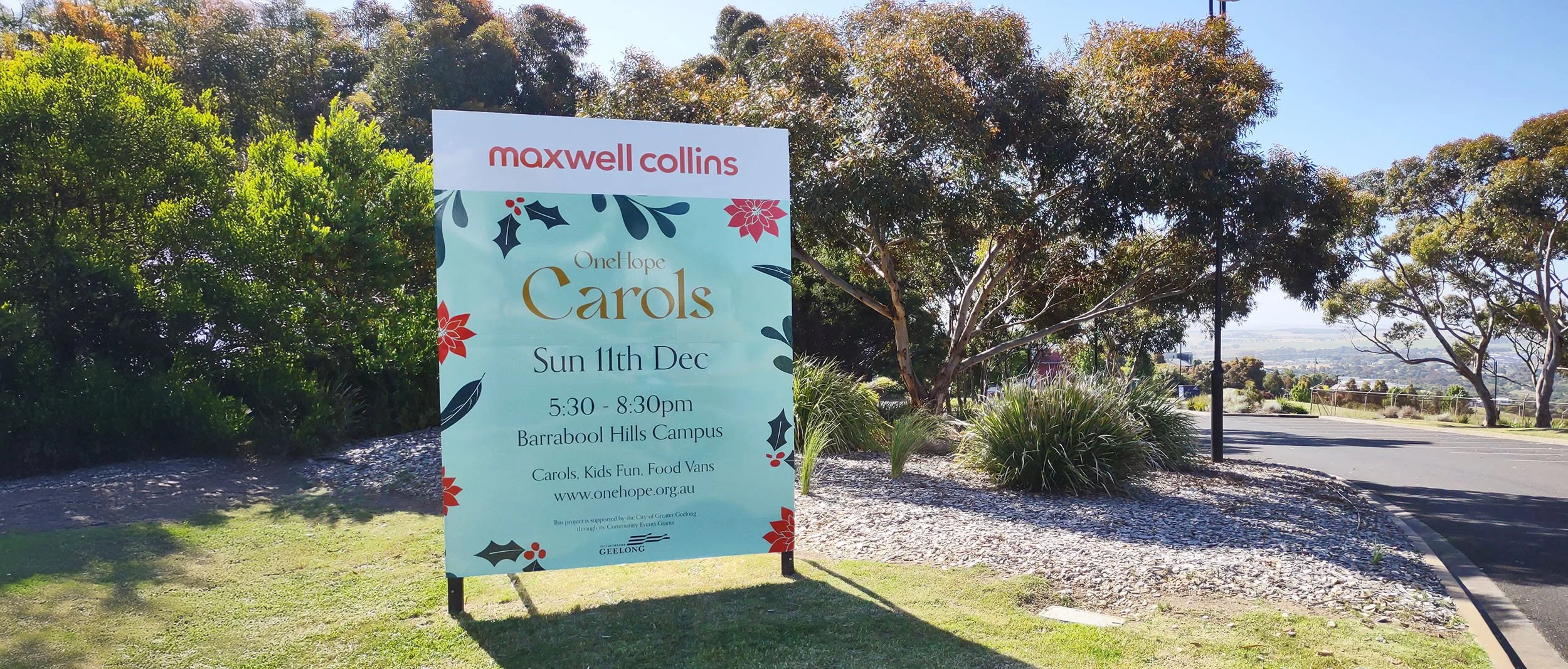 A small, outdoor, billboard-style sign advertising the OneHope Christmas Carols community event.