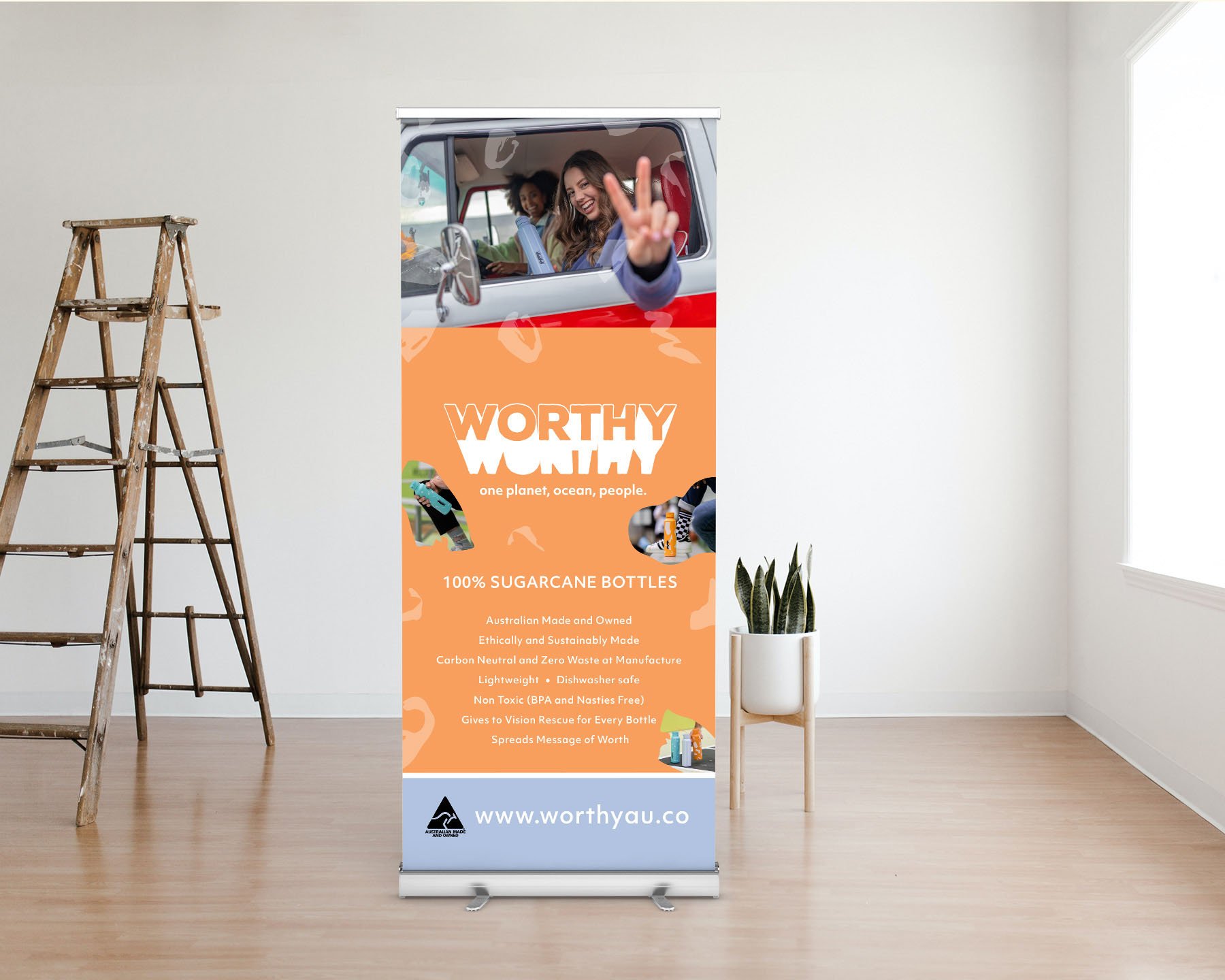 An orange pull-up banner in minimal room, advertising Worthy Co and their sugarcane drink bottles.