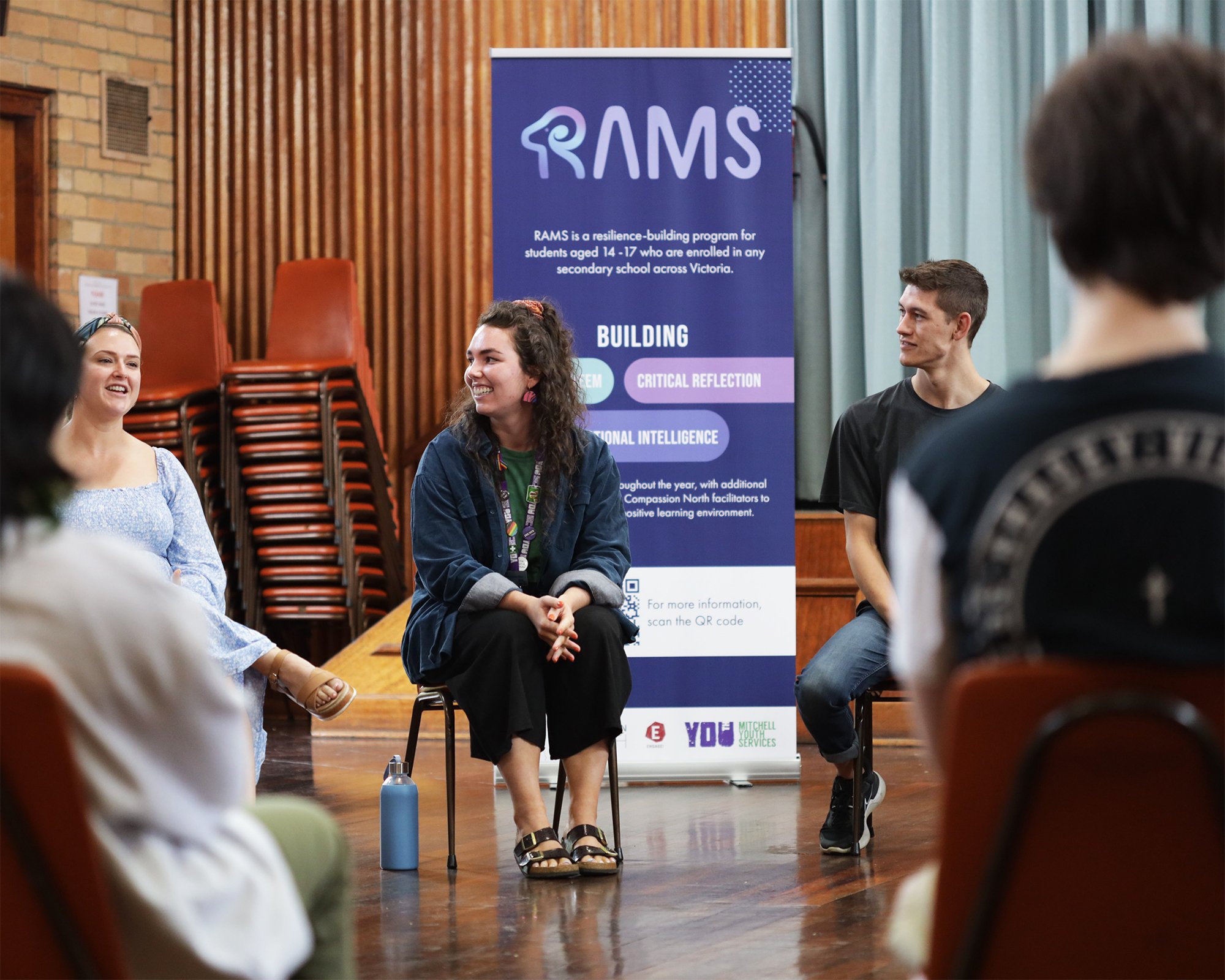 A group of RAMS program participants discussing in a circle, with a RAMS Pull-up banner in the background.