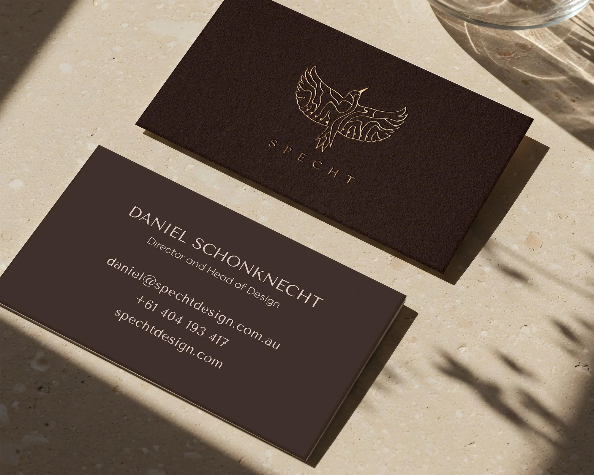 Front and back of brown Specht-branded business cards with gold foil logo.