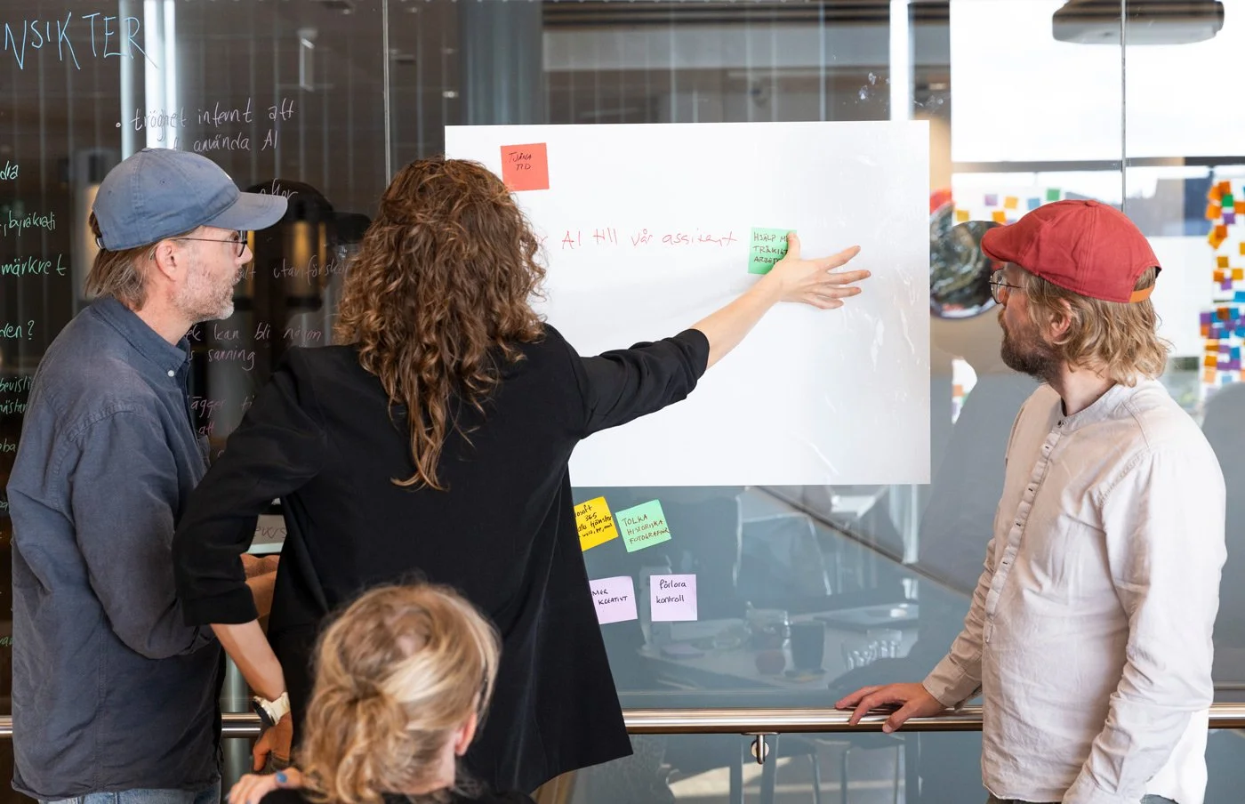 Fyra personer som diskuterar kring en whiteboard med post-it lappar i ett konferensrum.