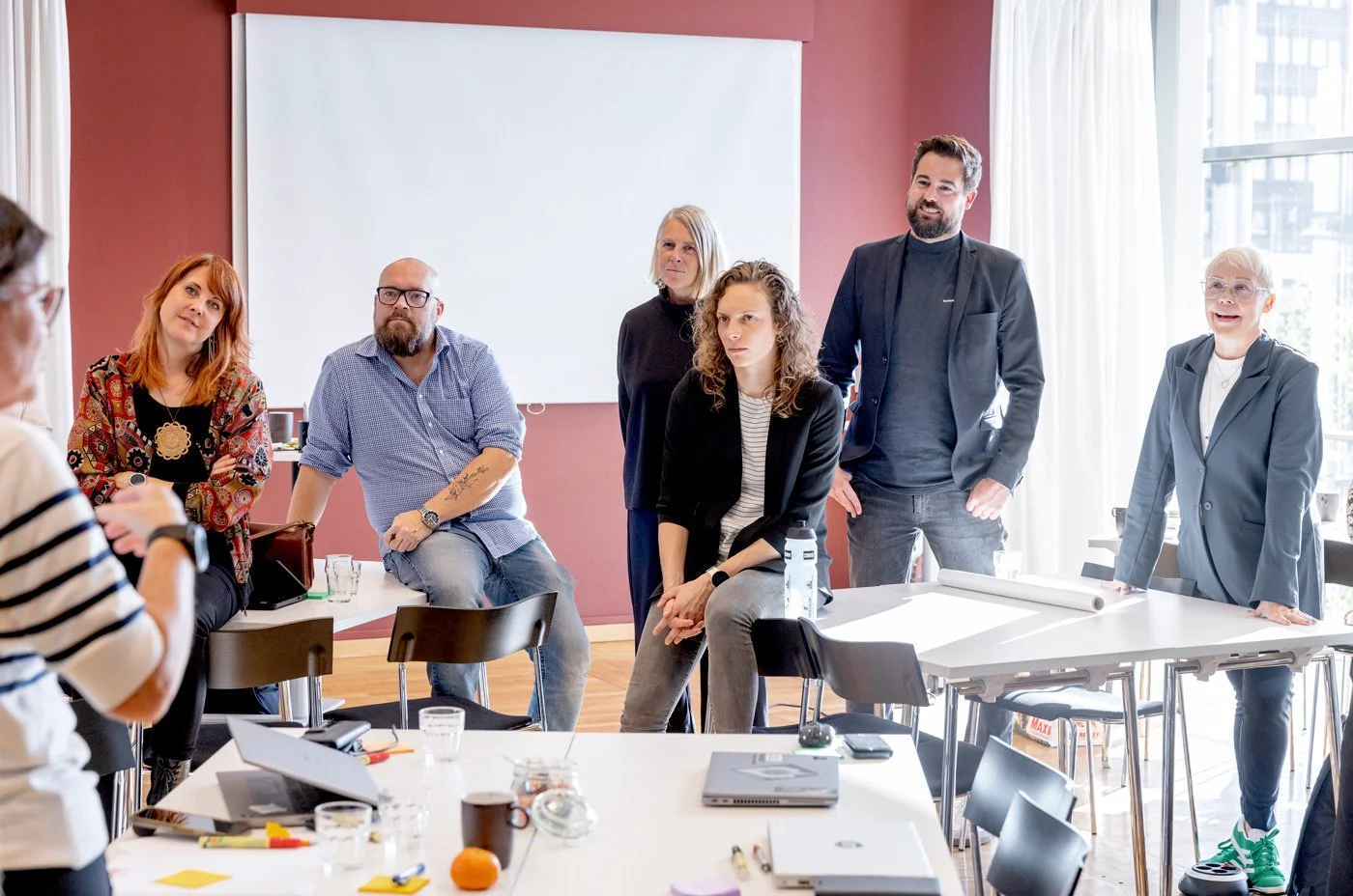 En grupp personer i ett mötesrum, några som står och några som sitter, deltar i ett möte.