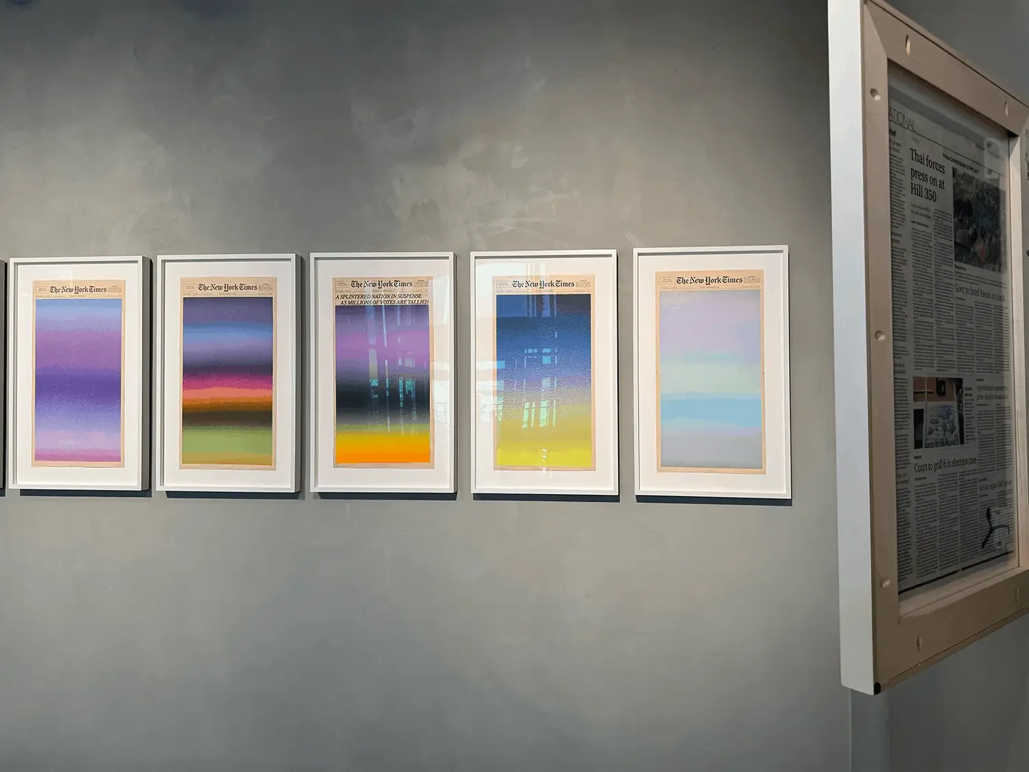 A row of framed sunrise paintings by Sho Shibuya from the Sunrise from a Small Window series, displayed on the second floor of Dib Bangkok, each painted on the front page of a newspaper