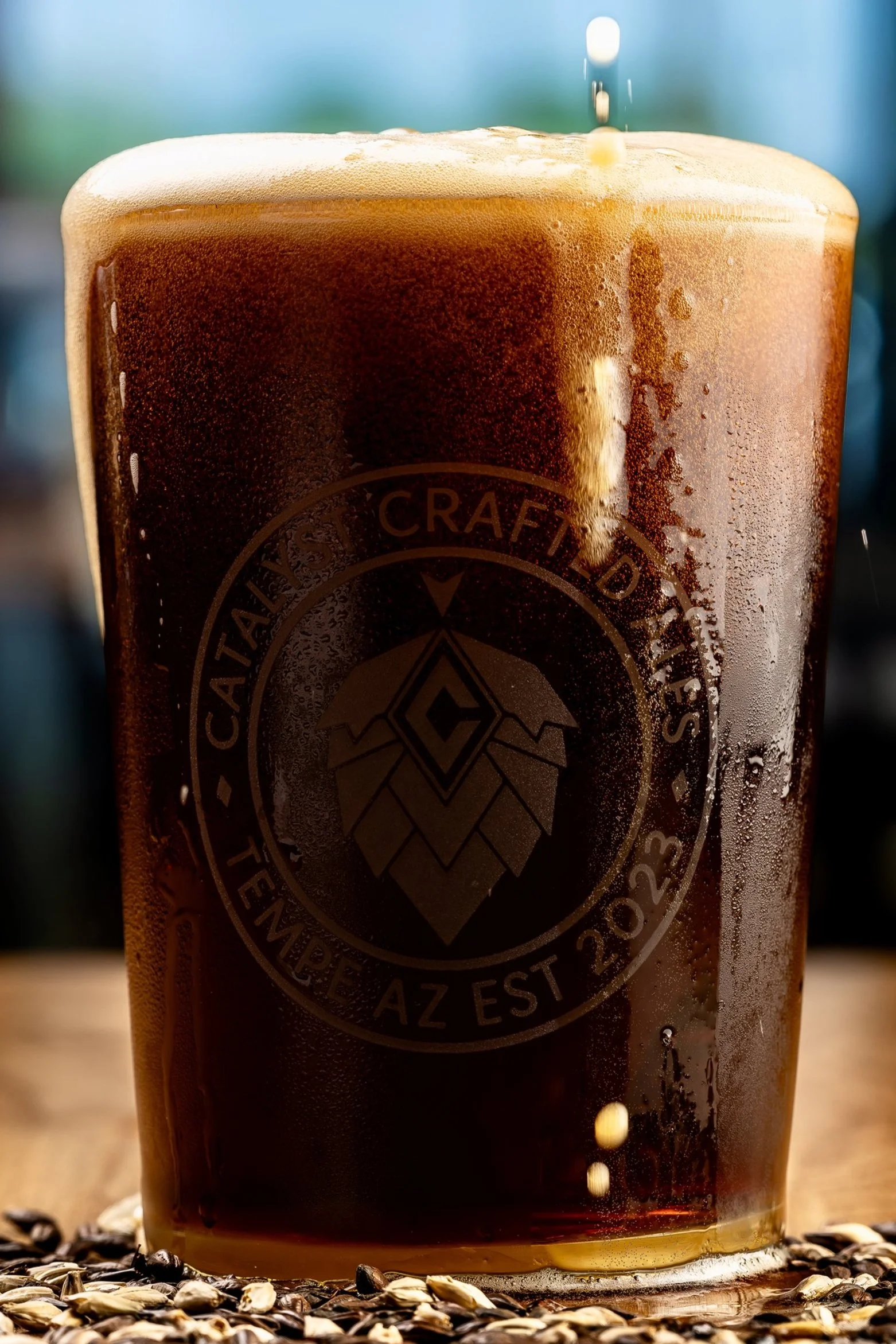 A close-up of a glass filled with a dark craft beer, with a head of foam and a logo etched on the side.