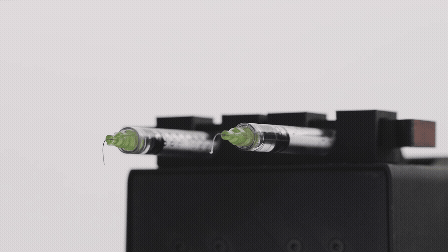 Two syringes filled with liquid resting on a black surface