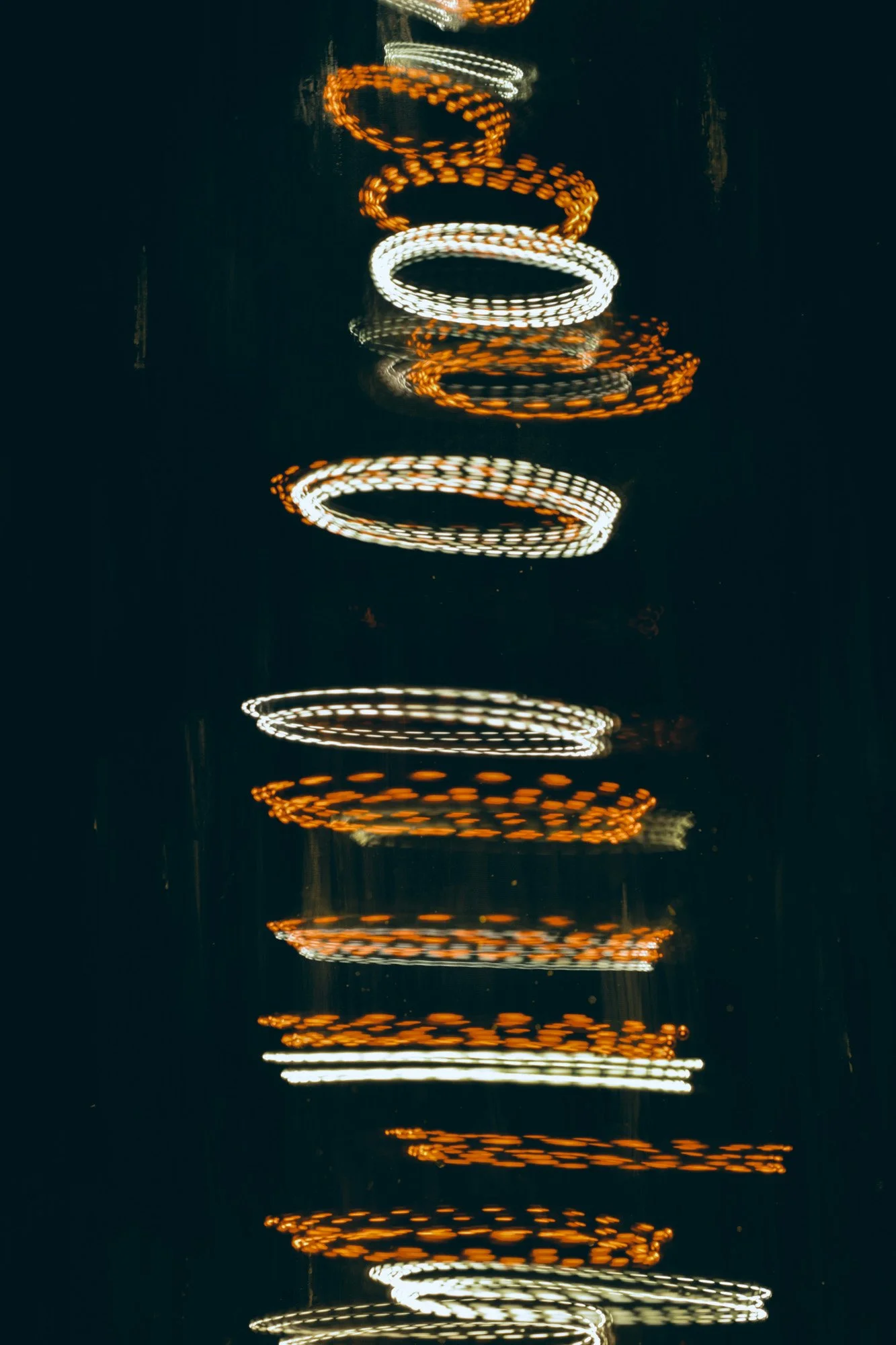 Vertical pattern of blurred, glowing orange and white circular lights reflecting on dark water at night.