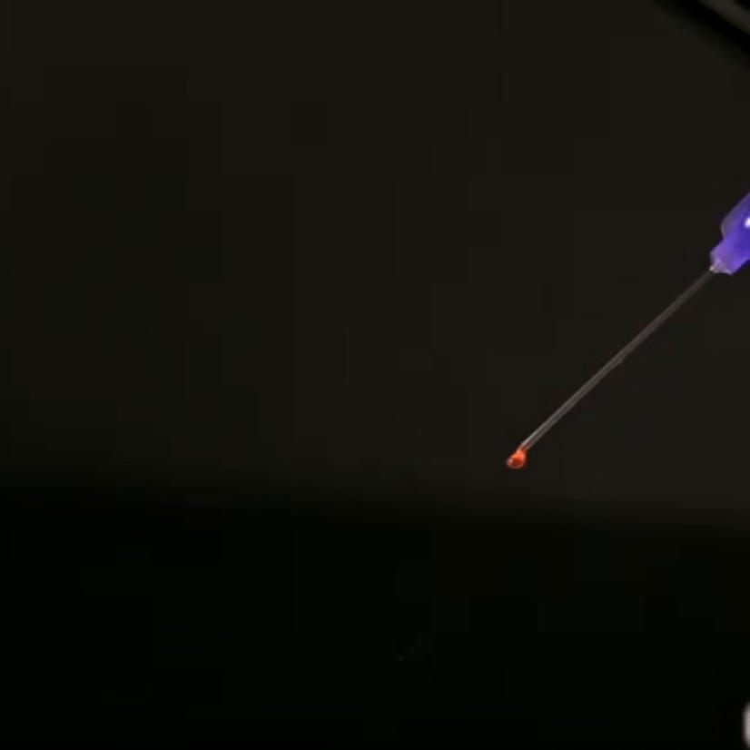 A dropper releases a small drop of red liquid onto a dark surface.