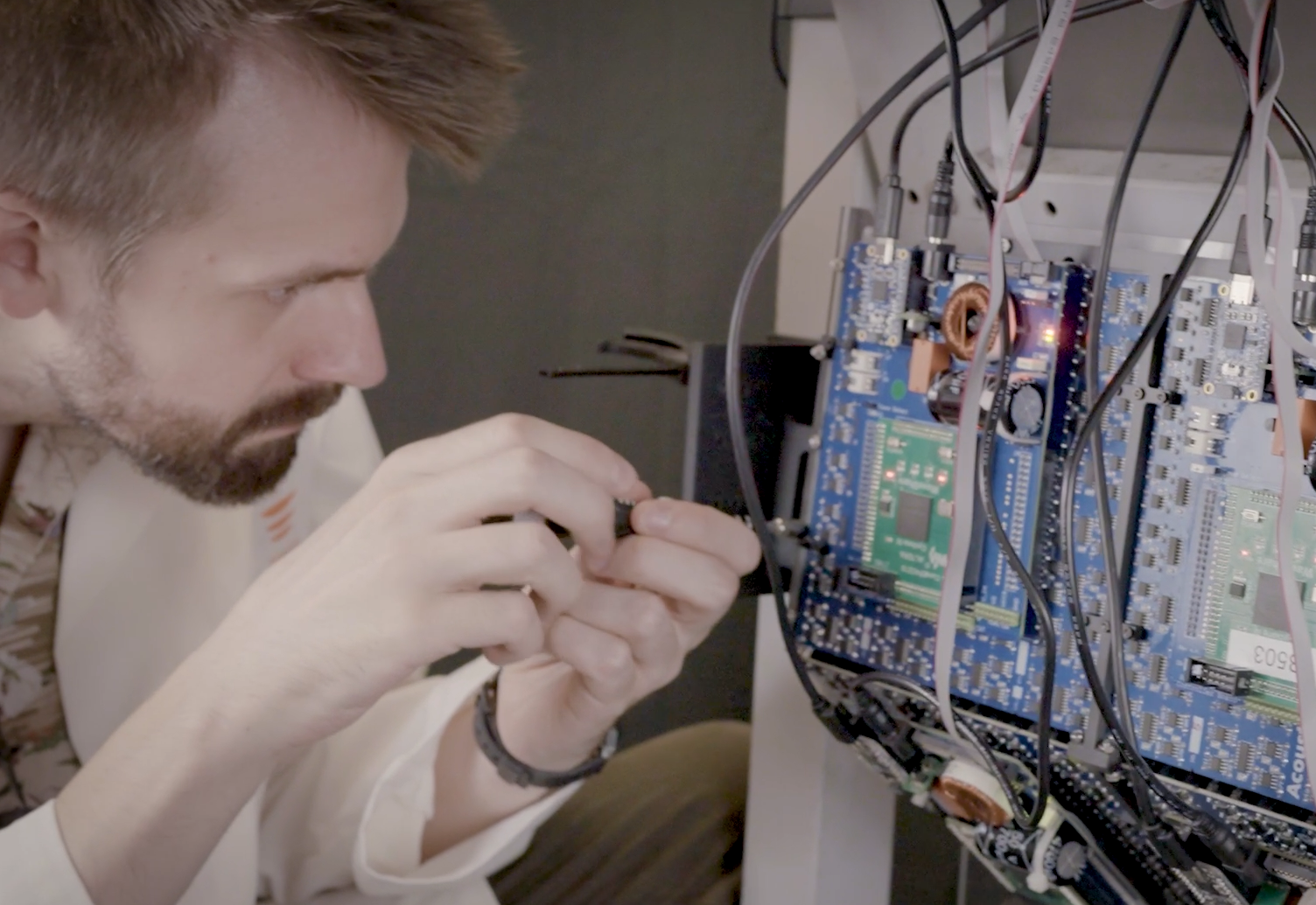 A man working with electronic components inside an open computer or electronic device, using a screwdriver to adjust or repair the circuit board with various wires and circuits.