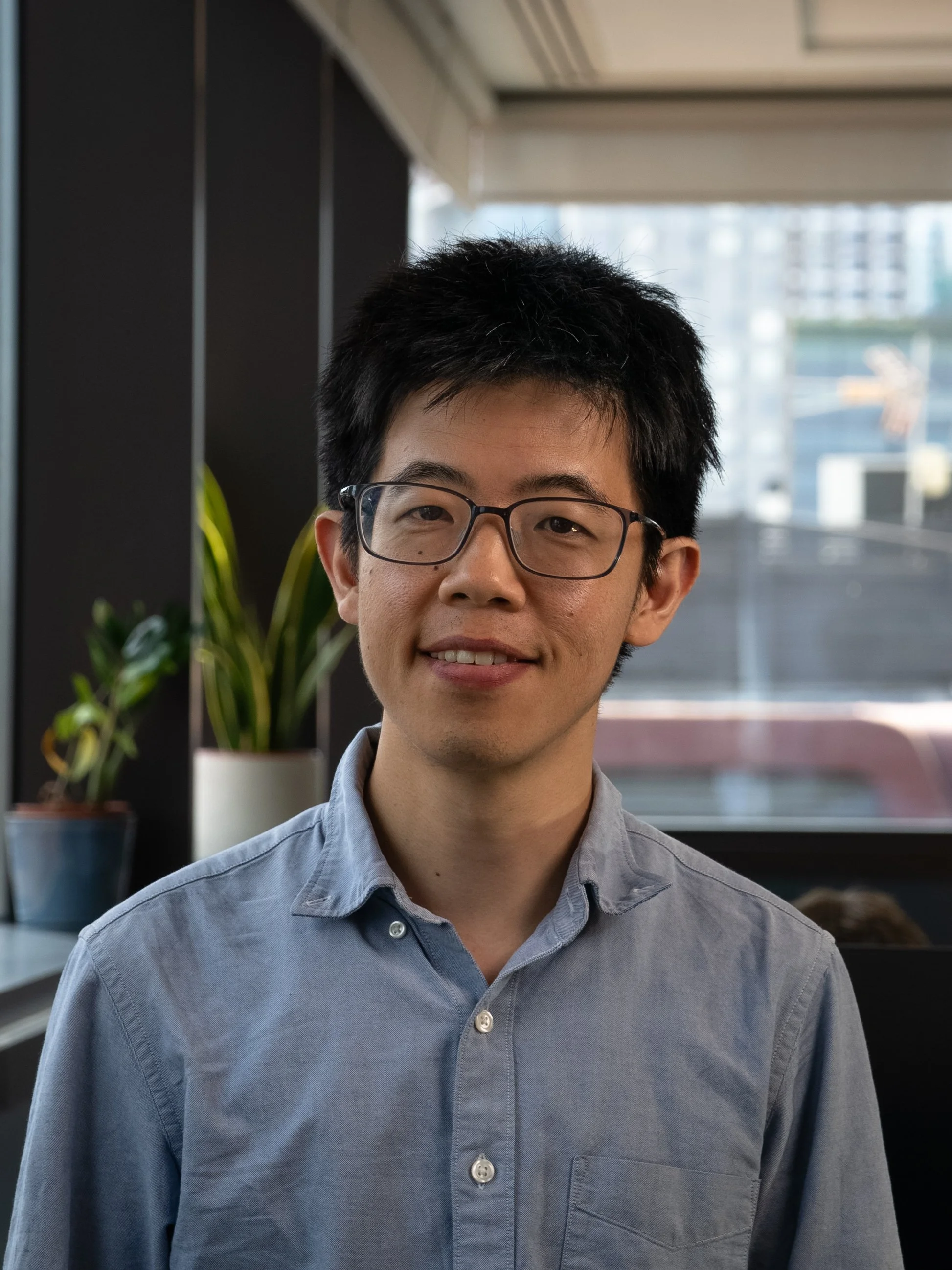 Black and white photo of a young Asian man smiling, with short straight hair and wearing a collared shirt.