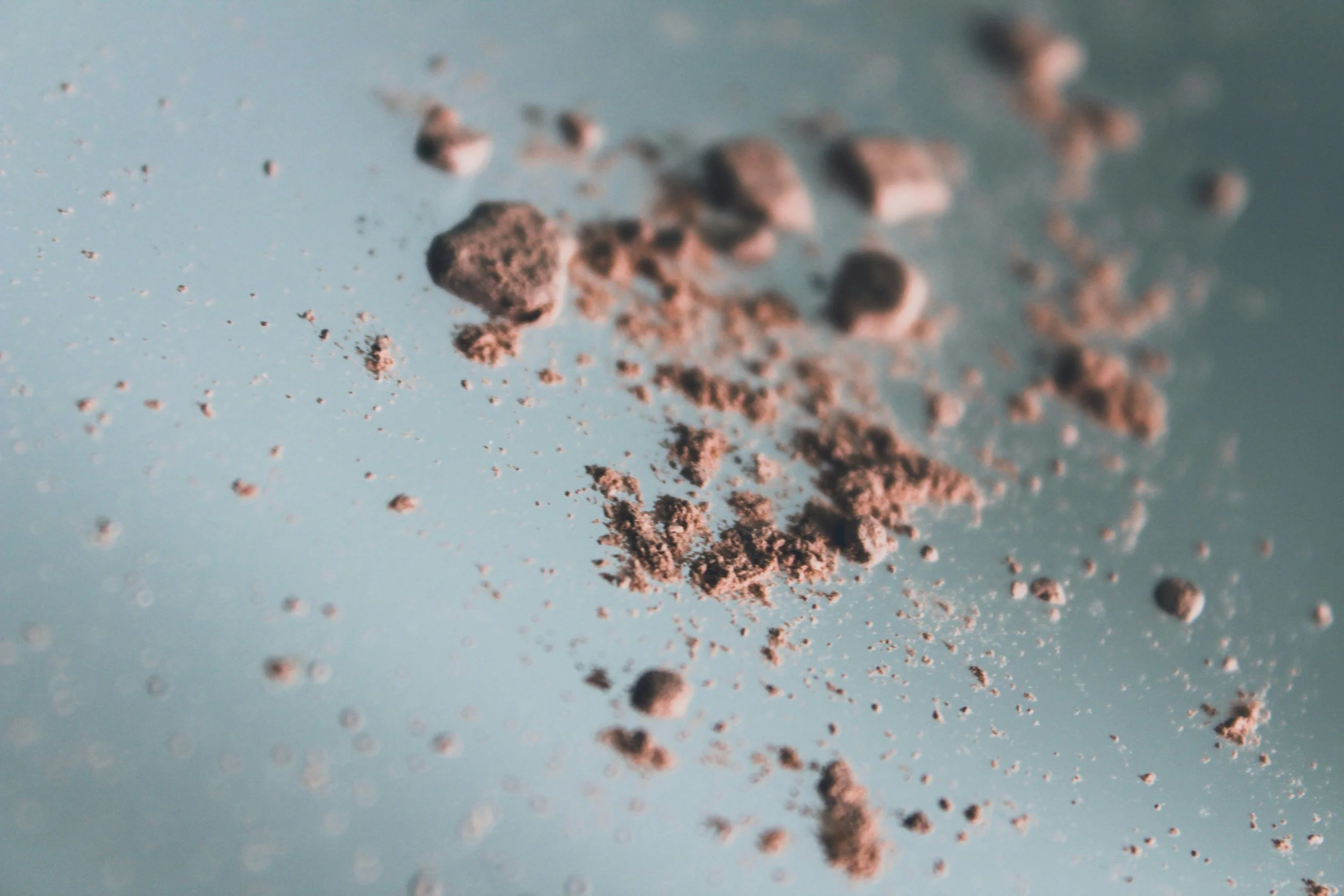 Close-up of scattered brown powder or dirt particles on a light blue surface.