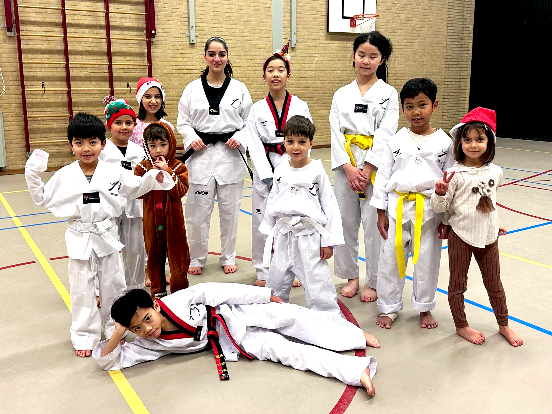 Group of children in taekwondo uniforms holding up festive treats and smiling, in a martial arts studio.