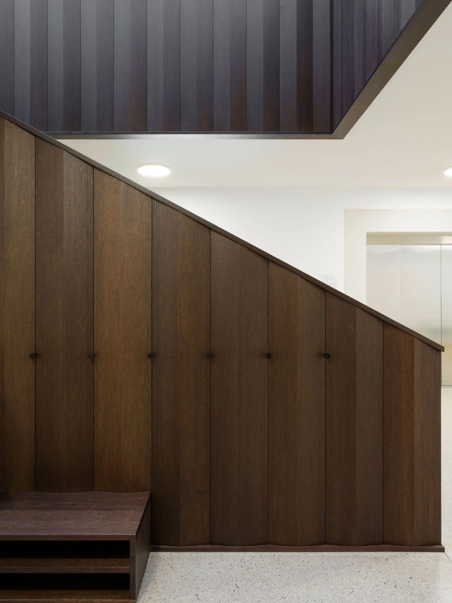 Parete di pannelli di legno scuri e chiari in ambienti interni con luci a incasso a soffitto.