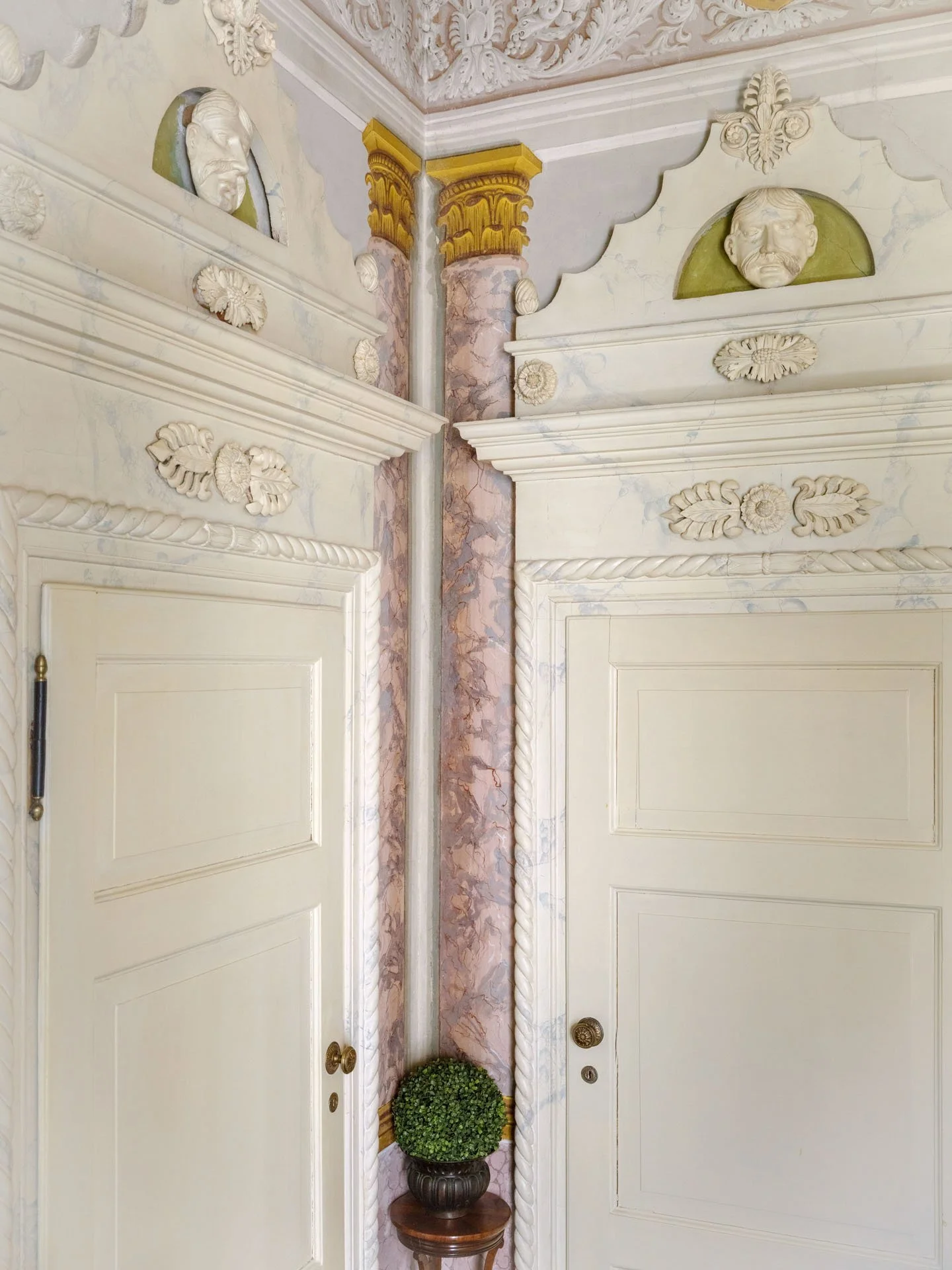 Decorata porta in stile classico con cornici in rilievo, rilievi artistici e maschere in pietra sulle pareti in marmo.