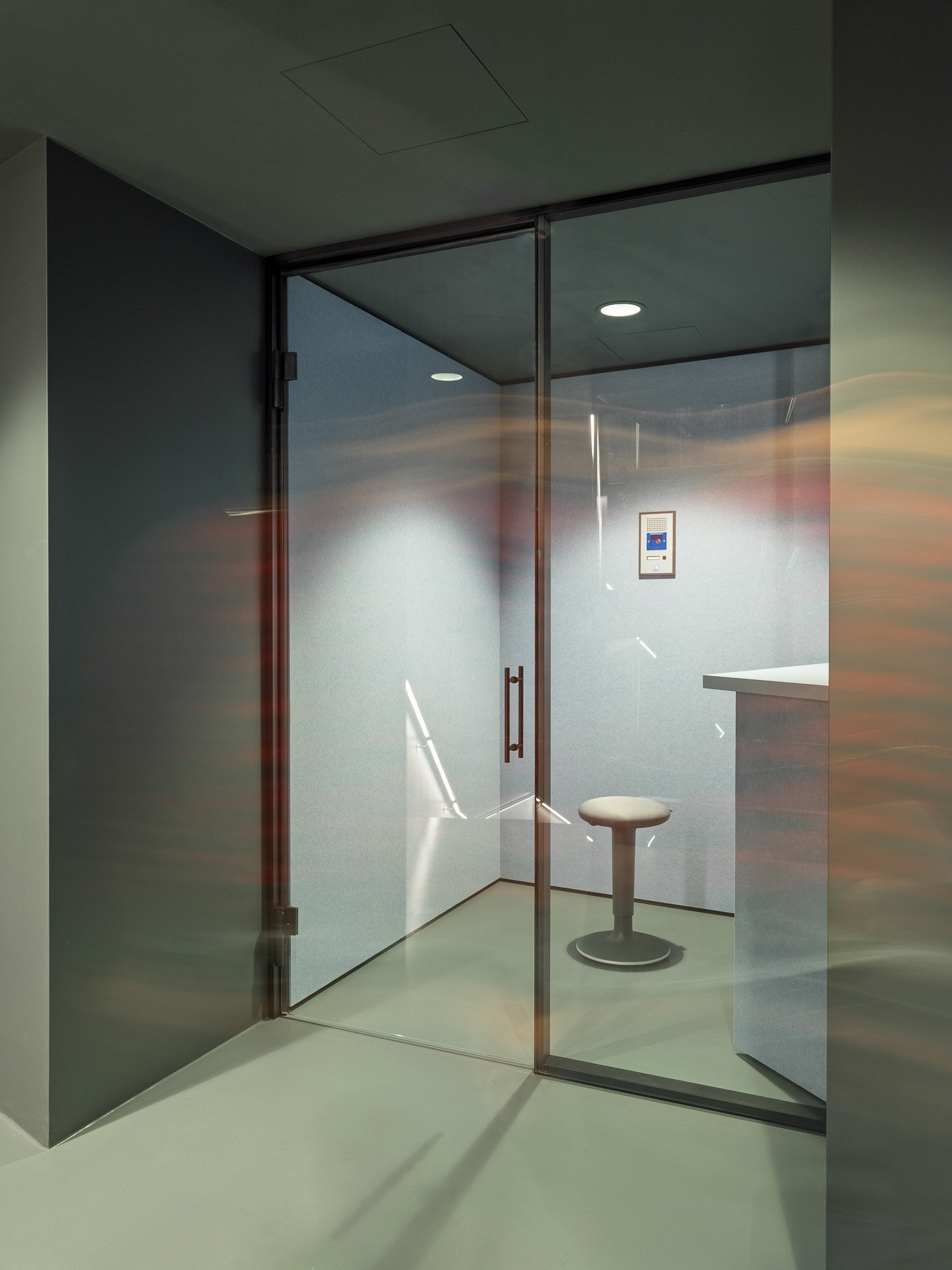 Stanza con pareti di vetro, sedia da visita medica, schermo e luci sul soffitto.
