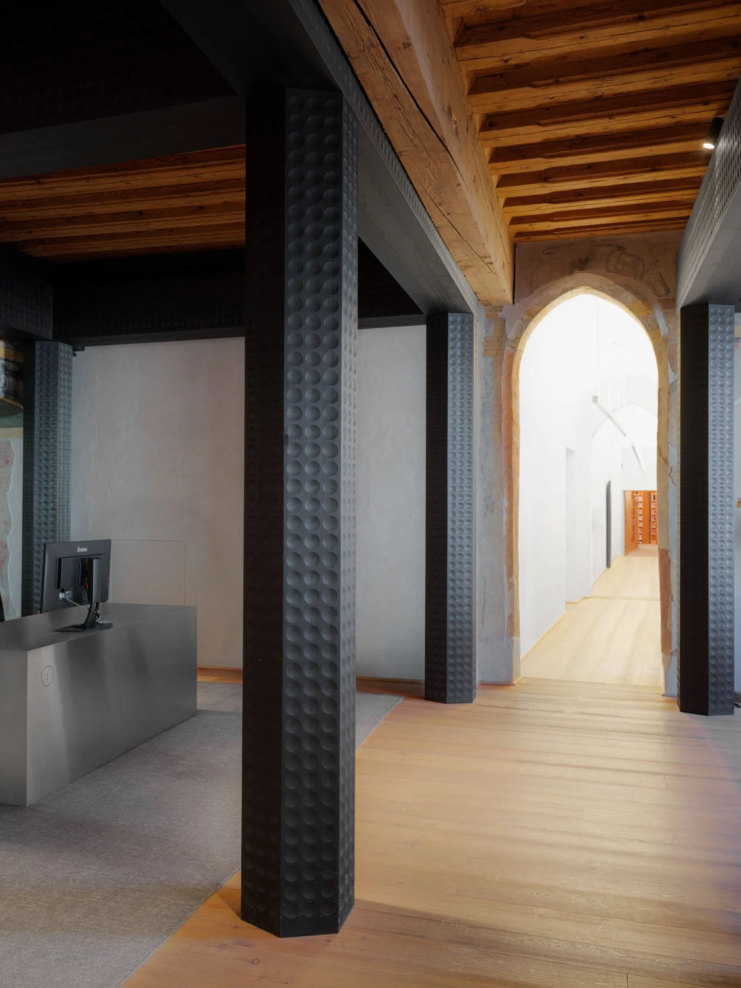 Interno di un edificio con colonne nere con superficie a sfera, pareti in pietra e travi in legno sul soffitto.