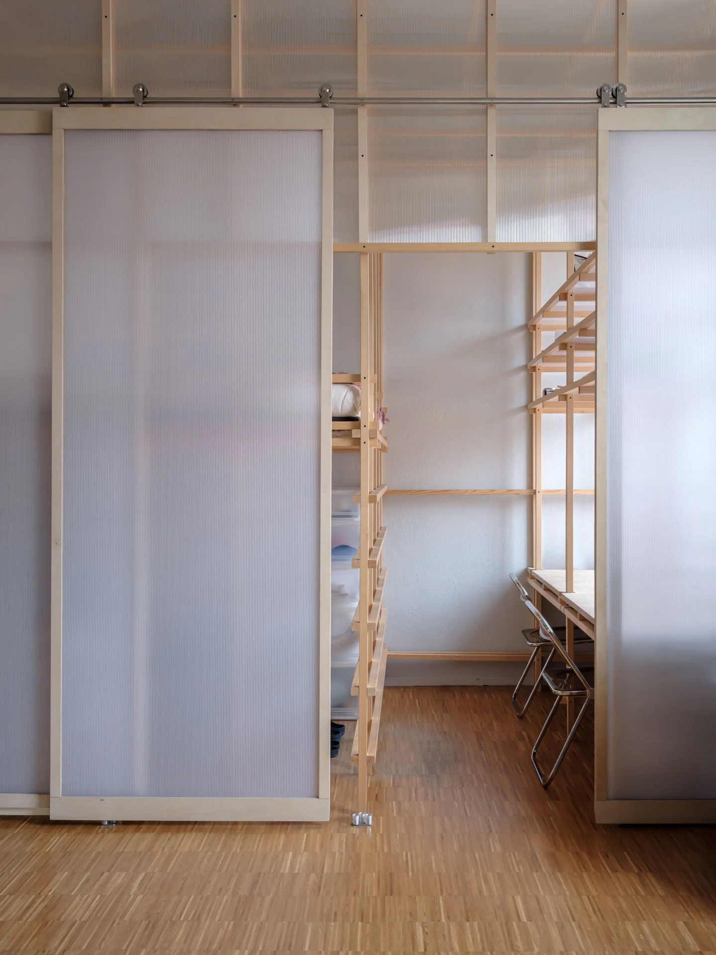Interno di una stanza con pareti in plastica trasparente e scaffali di legno, con sedie nere e un tavolo in un angolo.