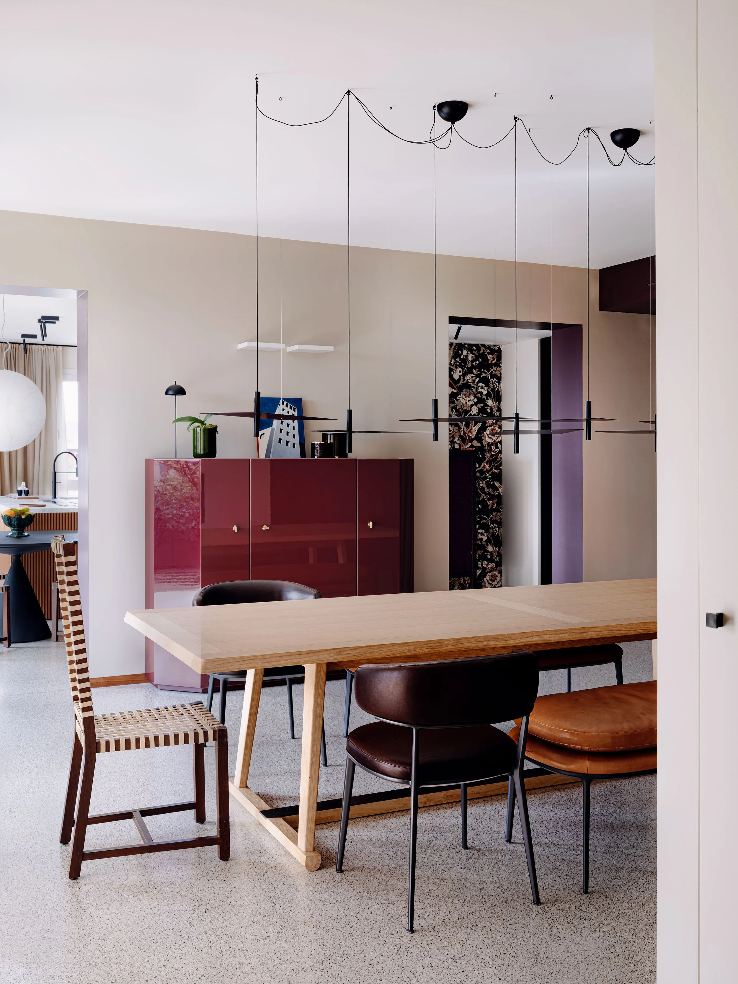 Interno di una casa moderna con un tavolo in legno, sedie di diversi stili, ambientazione con pareti beige e decorazioni moderne.