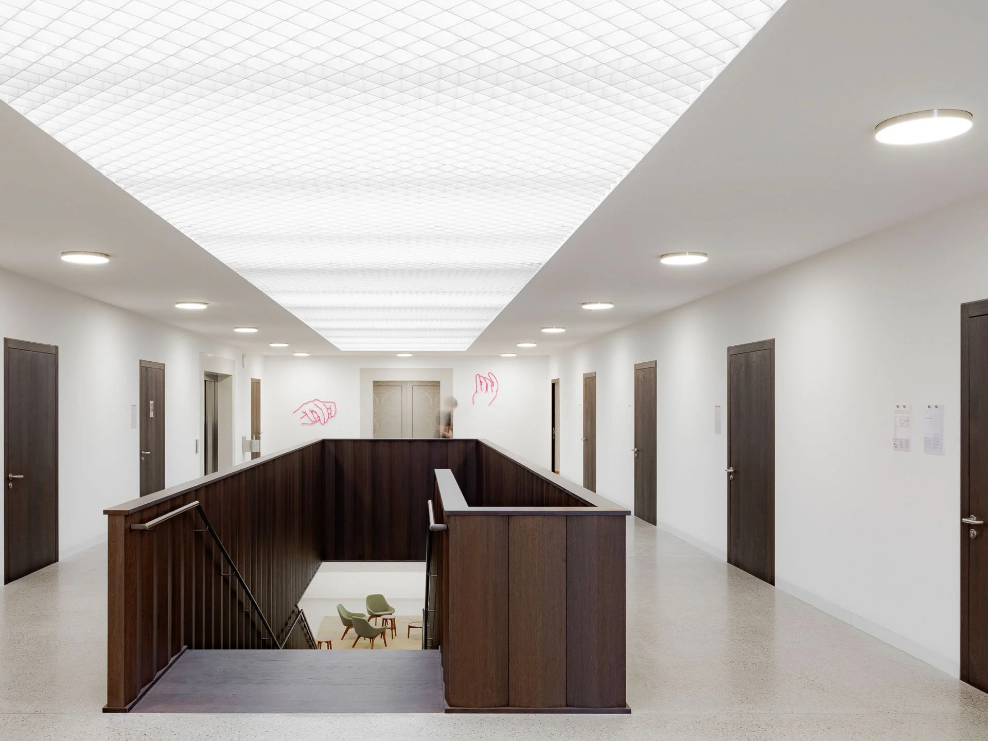 Interno di un edificio con corridoio, elevatore e area di attesa, soffitto con illuminazione a LED e pareti bianche