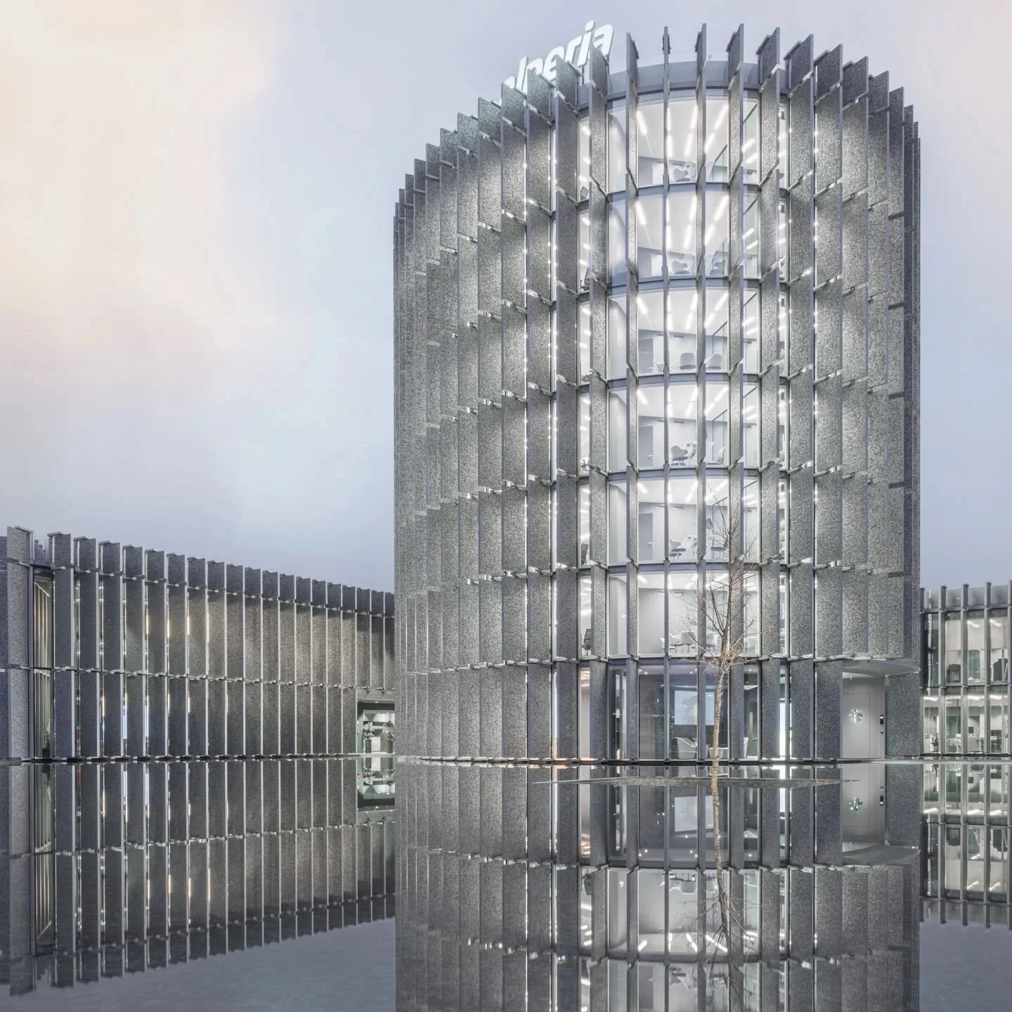Edificio moderno di vetro e metallo con illuminazione interna visibile attraverso le grandi finestre, riflettendo su una superficie d'acqua.