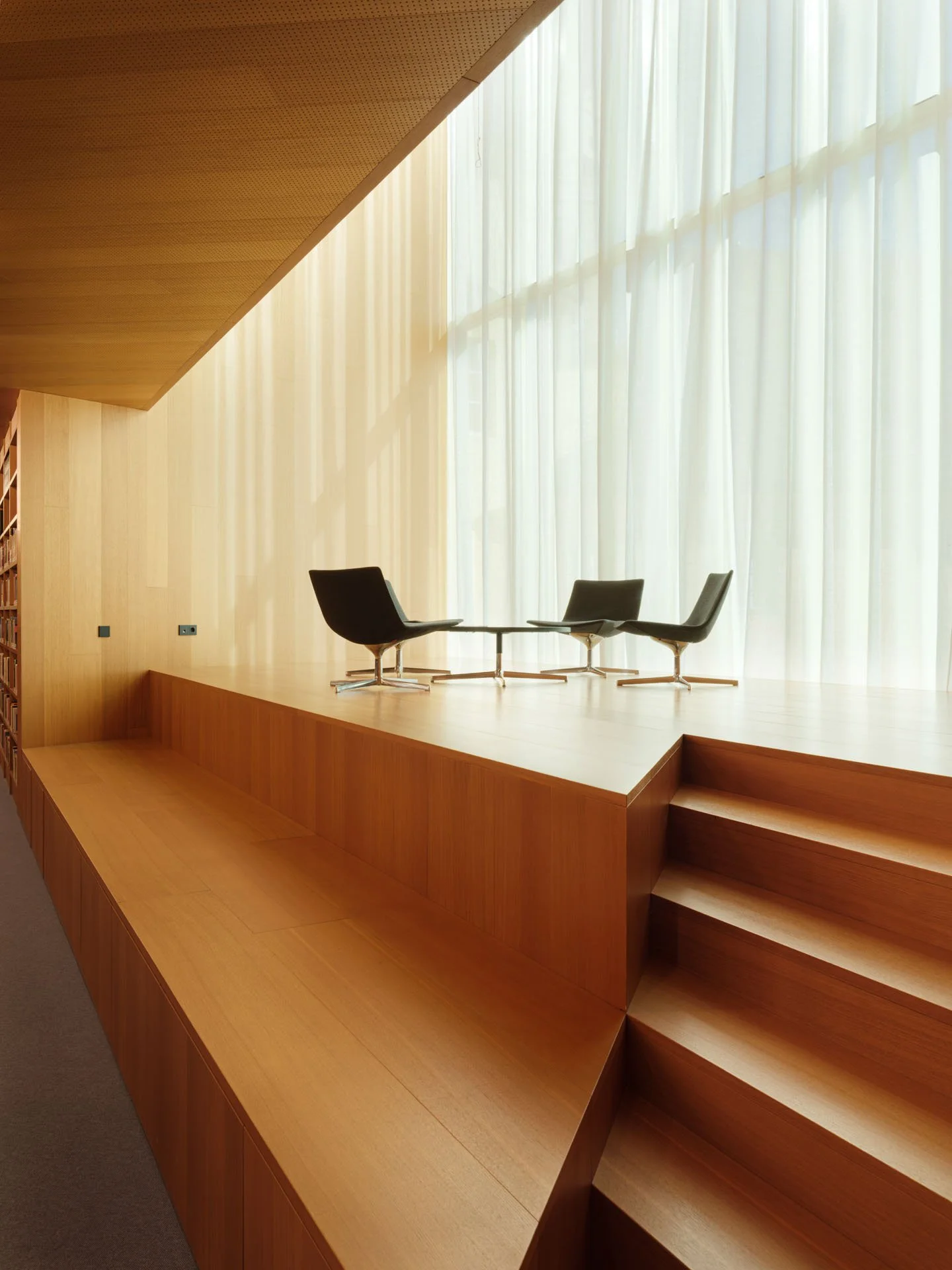 Spettacolare scena di un palco con sedie di design in legno e grandi vetrate che lasciano entrare luce naturale, caratterizzato da un soffitto in legno e atmosfera moderna ed elegante.