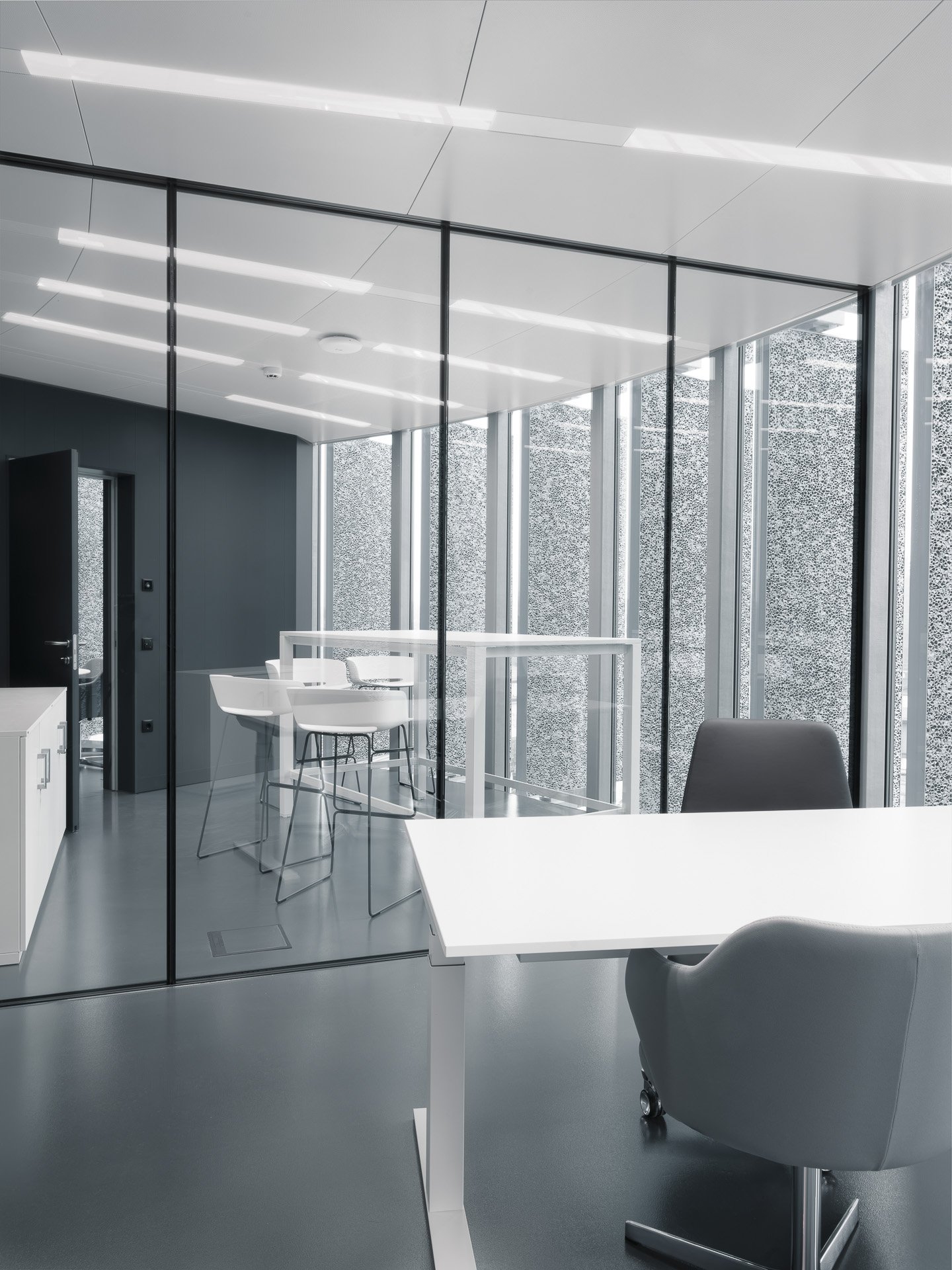 Interno di un ufficio moderno con pareti di vetro, scrivania bianca e sedie di design.