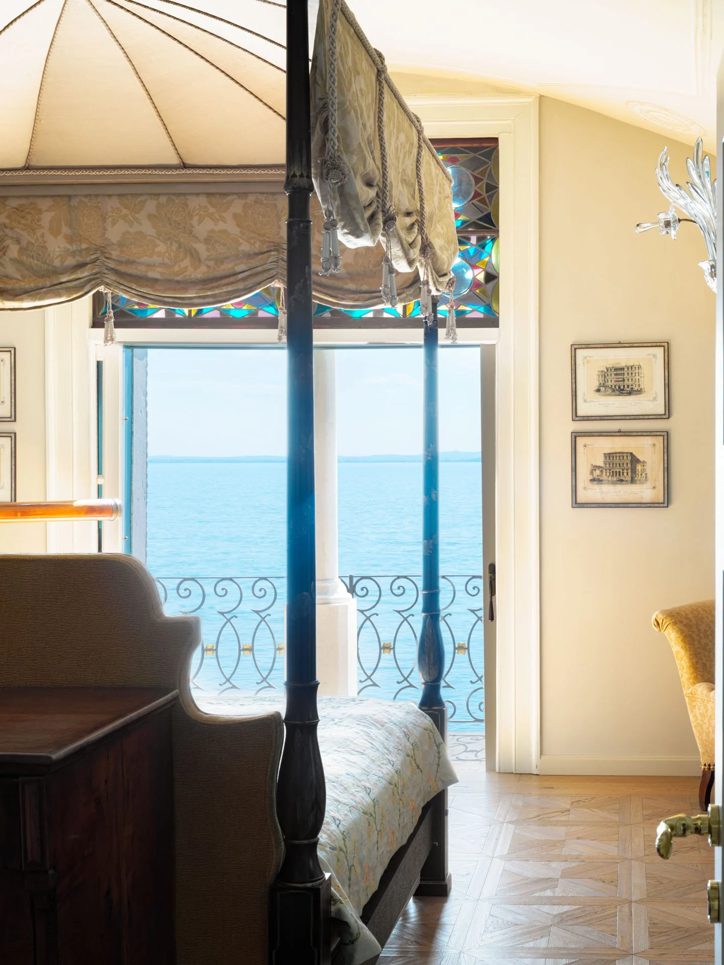 Camera con letto vista sul mare, con angolo arredato, una lampada a lampadario, finestre con vetri colorati e pareti decorate con quadri.