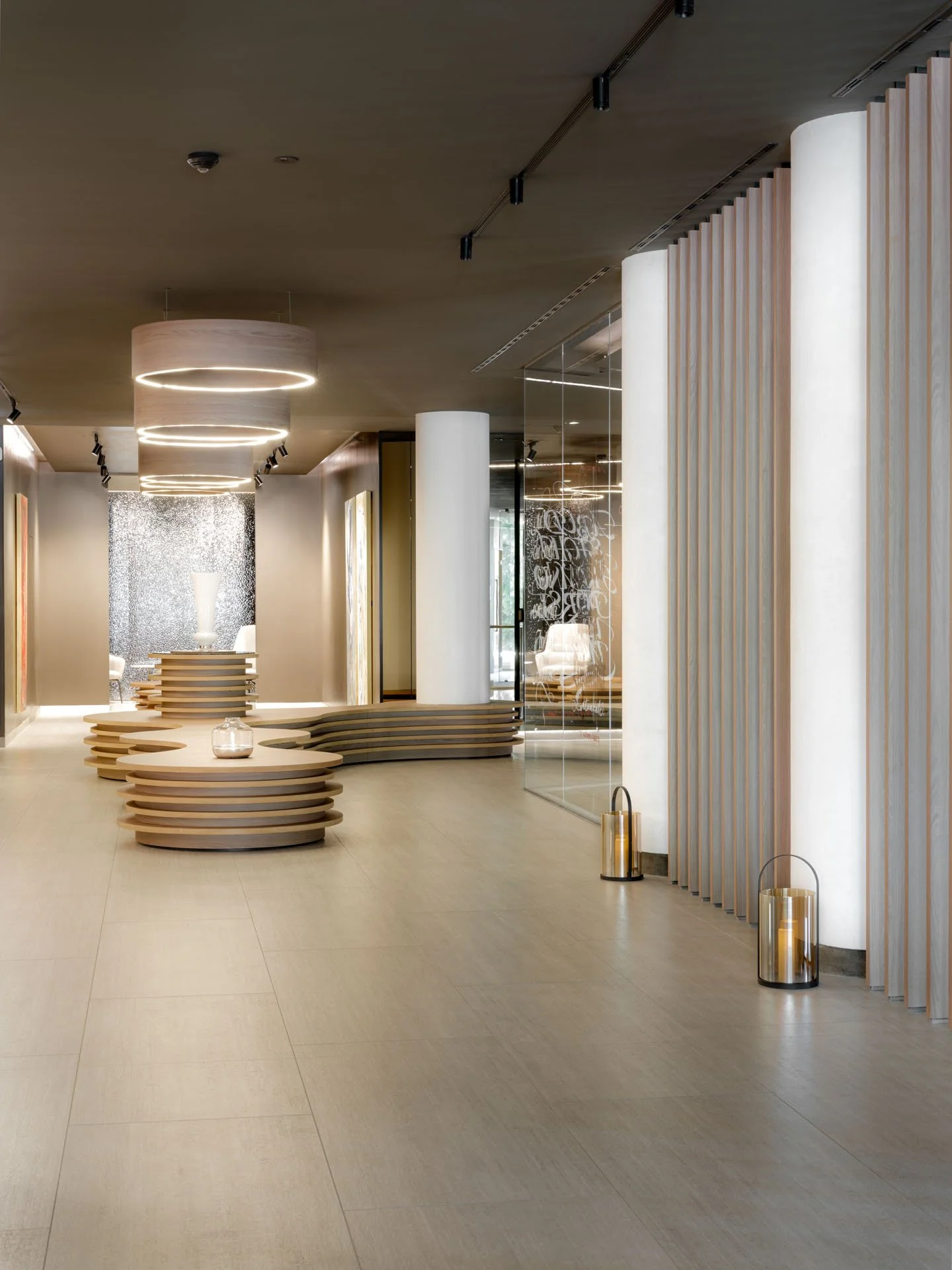 Interno di un edificio moderno con arredo minimale e luci sospese; pavimento chiaro, pareti con pannelli di legno e display di vetro.