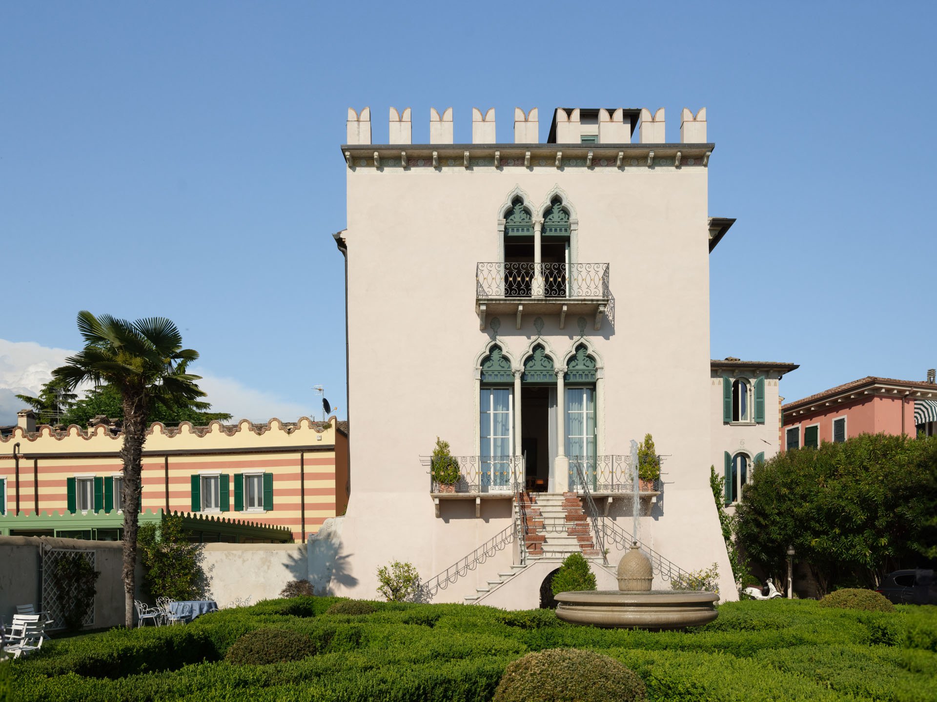 Edificio bianco con balcone e finestre ad arco, scale esterne e giardino con panchine e fontana