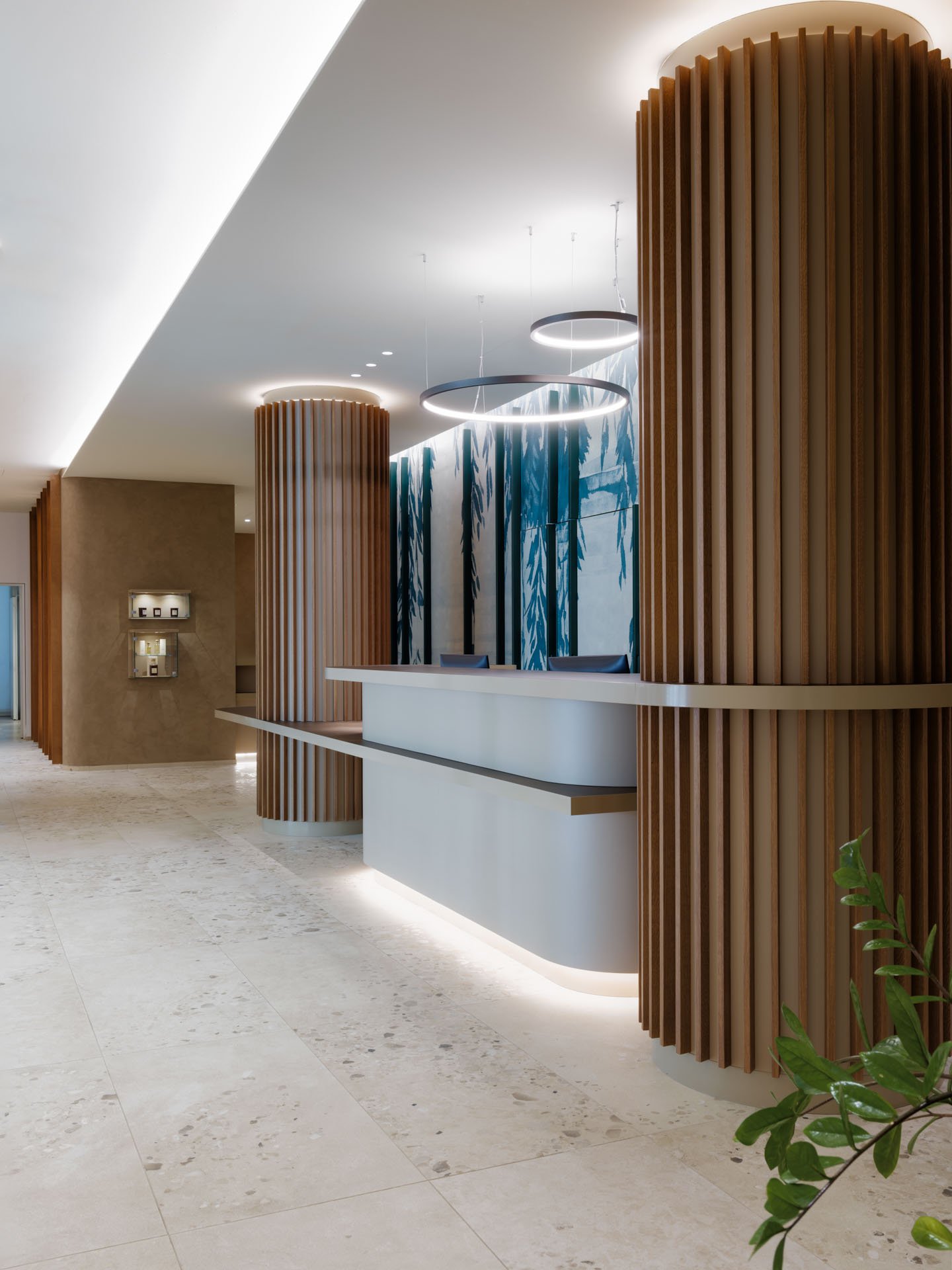 Reception area con mobili in legno curvato e luci circolari sospese, pareti decorate con fantasia di foglie blu e verdi.