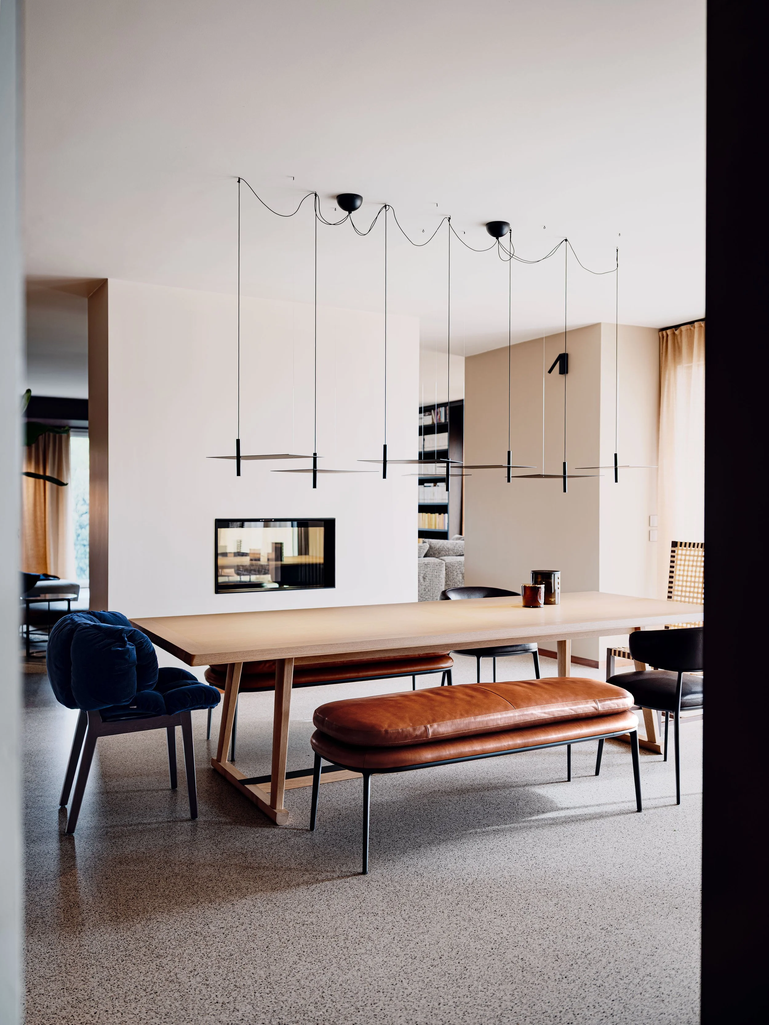 Interno di una casa con tavolo in legno, sedie blu e marrone, divano arancione, lampadario moderno e pareti chiare