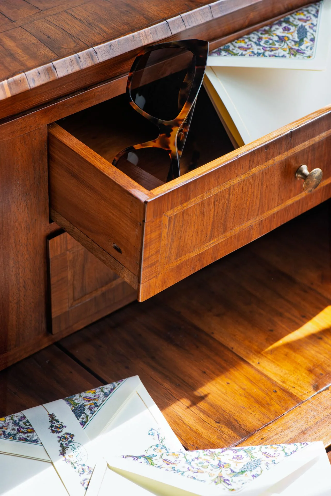 Occhio di un cassetto di legno con un paio di occhiali da sole tartarugati e una rivista aperta con pagine di decorazioni floreali.