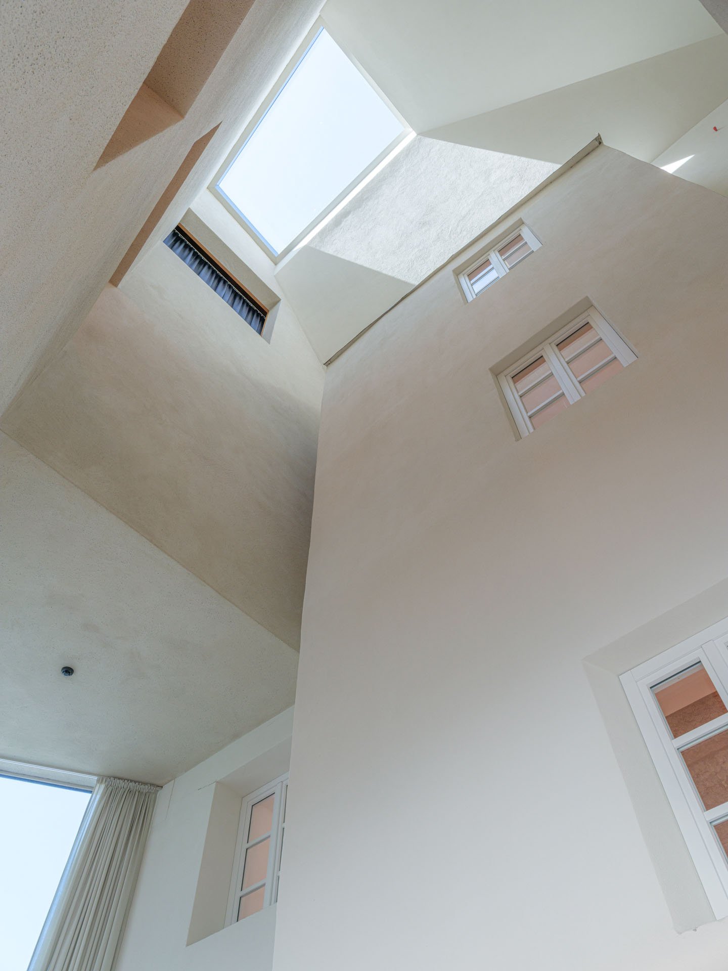 Interno di una stanza con pareti bianche, quattro finestre e un lucernario sulla soffitta.